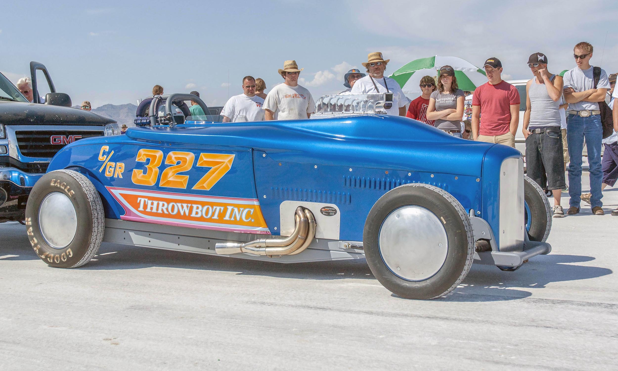 A blue roadsterwith the number 327 and the words Throwbot Inc. on the side, surrounded by spectators at Bonneville on a sunny day.