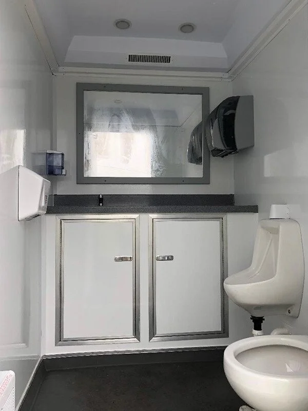A compact restroom with a urinal on the right and a cabinet with a granite countertop, a mirror, and soap dispenser on the left.