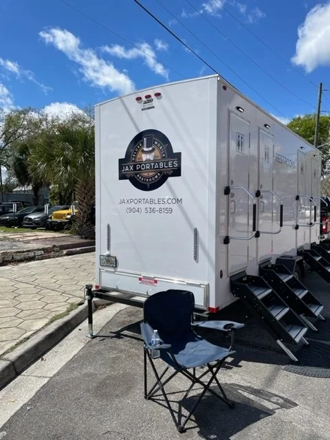 White portable event trailer with the logo and website for Jax Portables, and a folding chair placed in front of it in a parking lot.