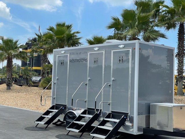 Portable restrooms set up outdoors with palm trees and a blue sky in the background.