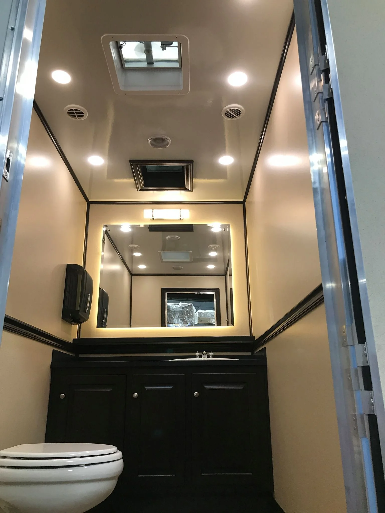 Bathroom with black vanity, sink, mirror with backlight, and ceiling vent, beige walls, and a white toilet in the corner.