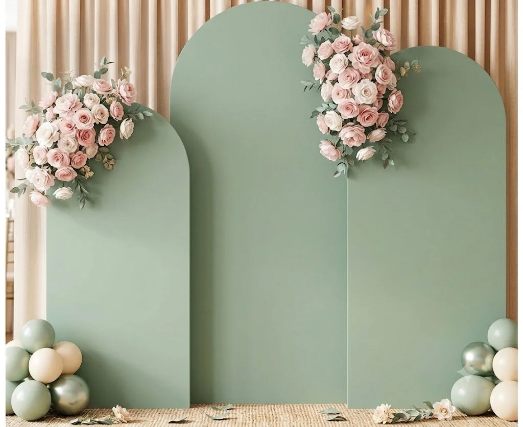 A decorative backdrop with three large green panels adorned with pink and white roses and eucalyptus, surrounded by pastel-colored balloons, on a wooden slat wall.