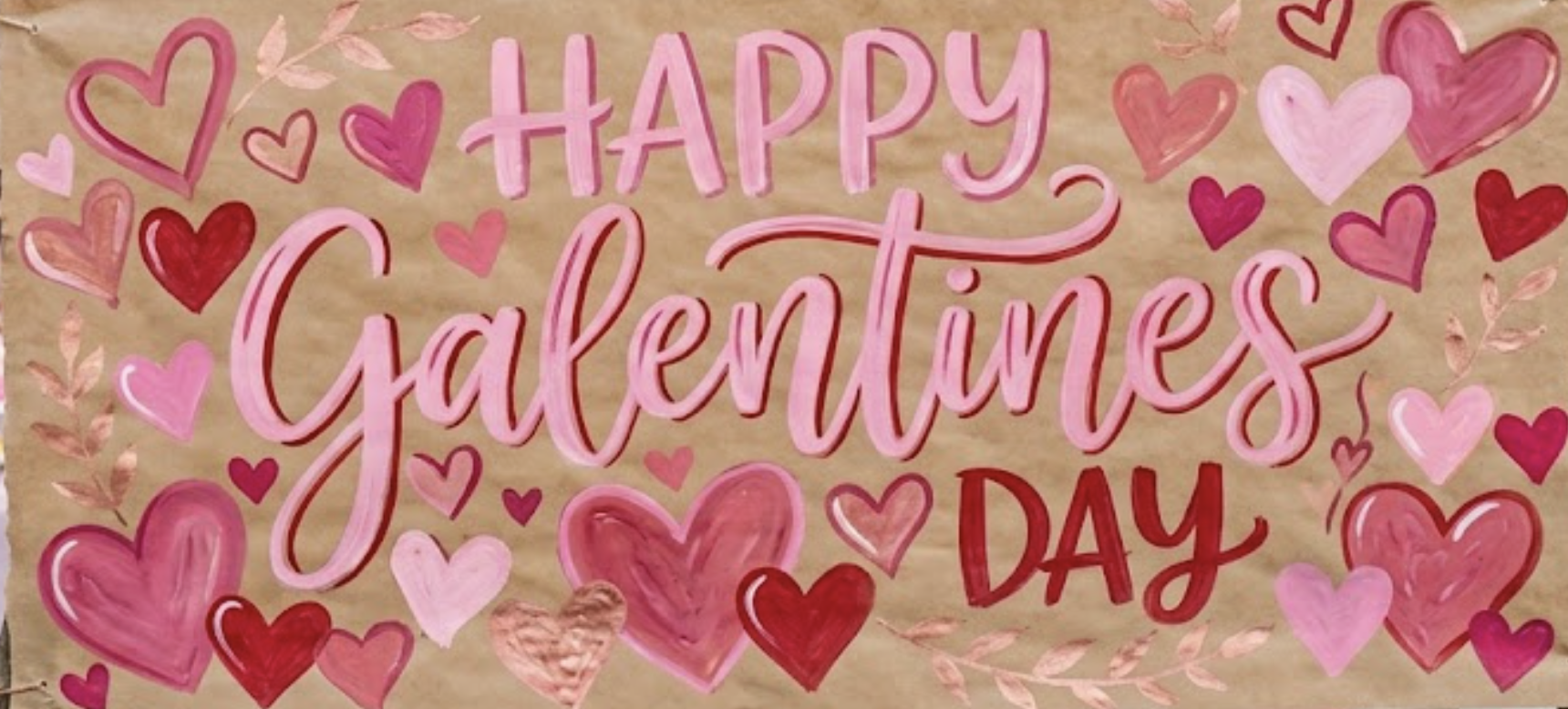 A colorful hand-drawn Valentine's Day poster with the message "Happy Galentines Day" surrounded by pink, red, and purple hearts and decorative leaves on a brown background.