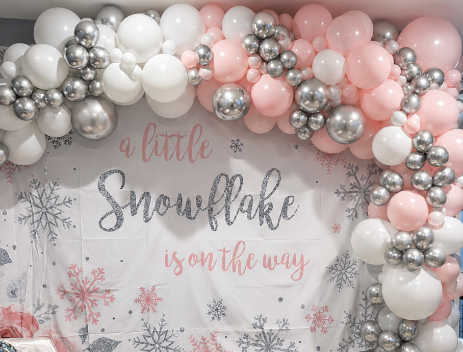 Balloon decoration with pink, white, and silver balloons around a sign that reads 'a little Snowflake is on the way,' with snowflake designs.