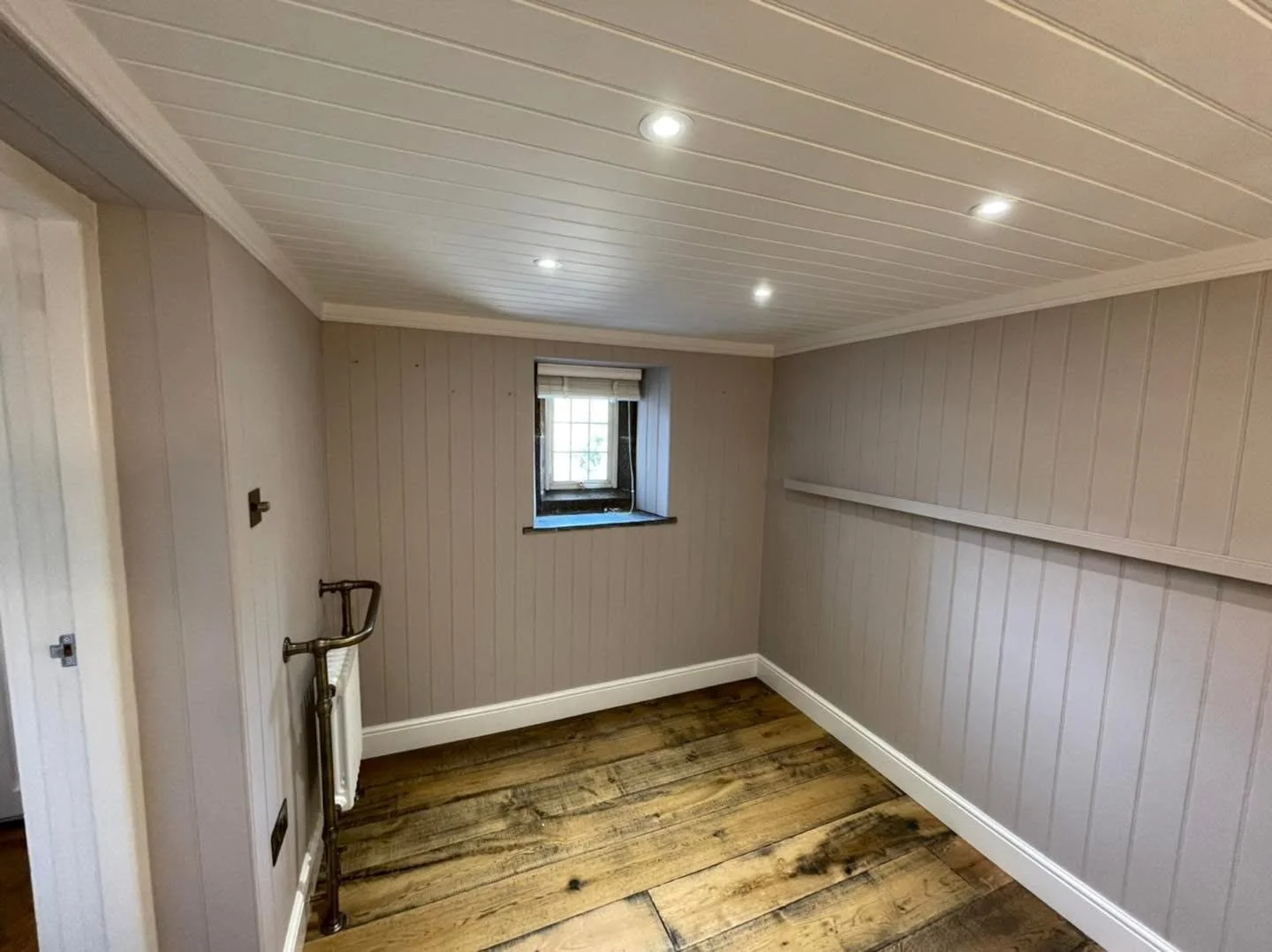 Small empty room with a window, wood plank flooring, and beadboard wall paneling, with recessed lighting in the ceiling.
