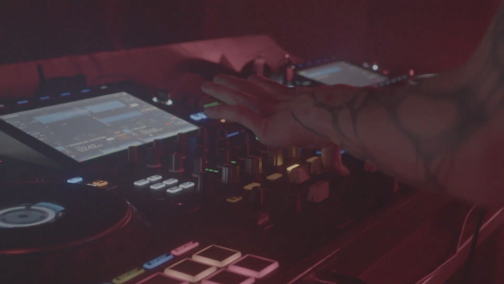 Close-up of a DJ's hand adjusting controls on a digital DJ controller in a dark setting with red and blue lighting.