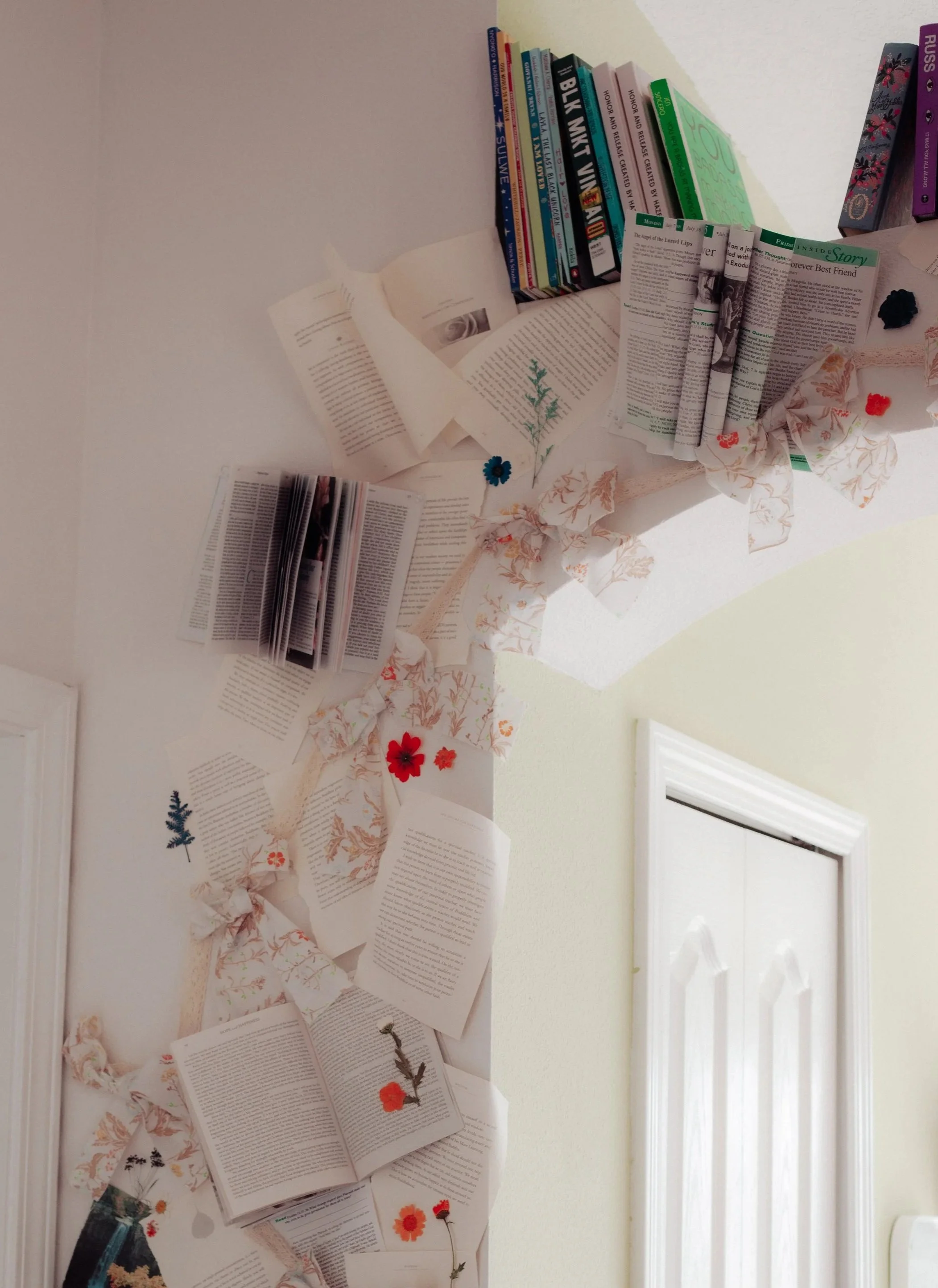 A creative wall decor display with open books, magazines, and decorative paper flowers and leaves arranged on a beige wall.