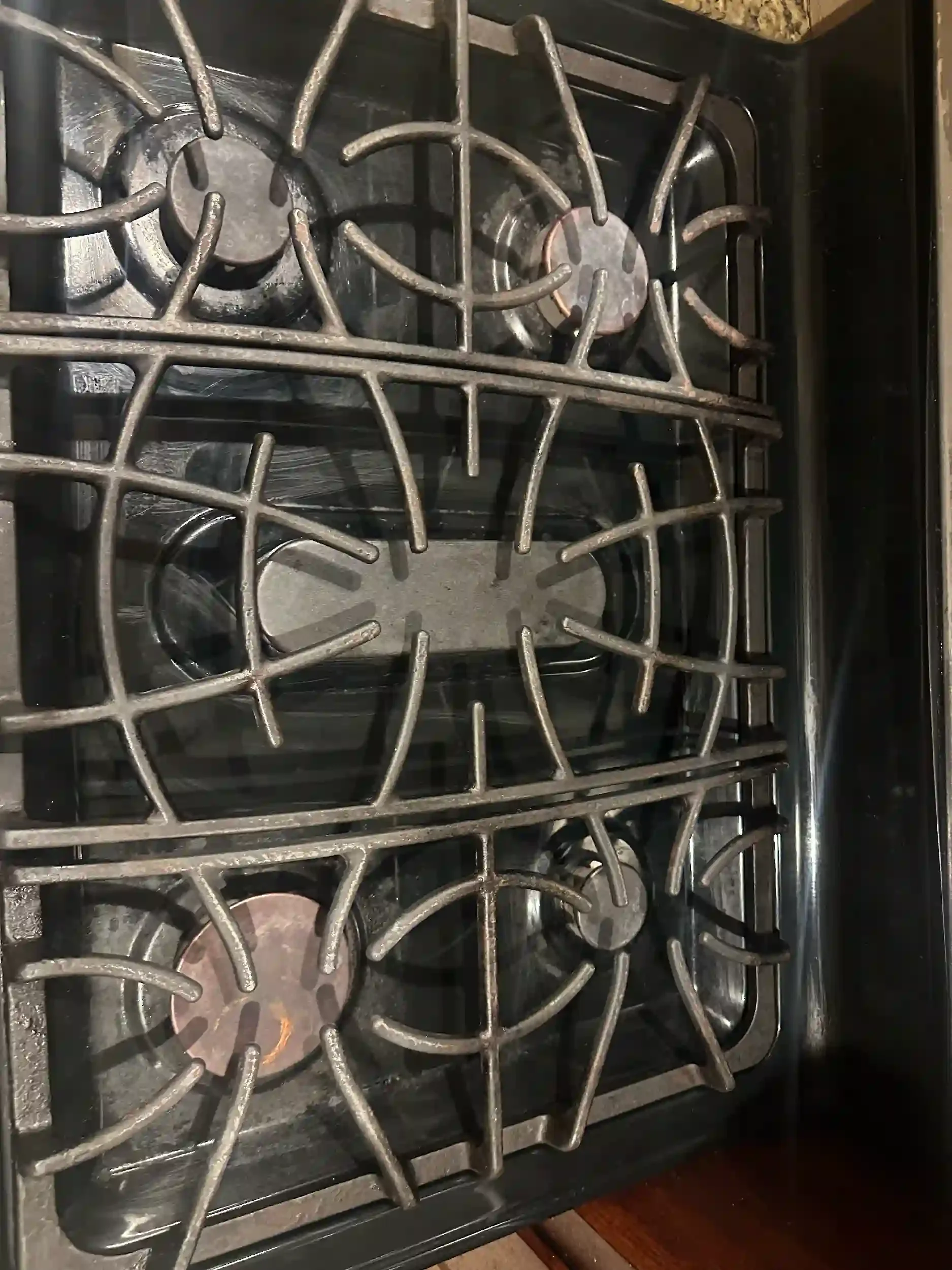 Close-up of a gas stove with multiple burners and cast iron grates, some burners showing signs of use with slight discoloration.