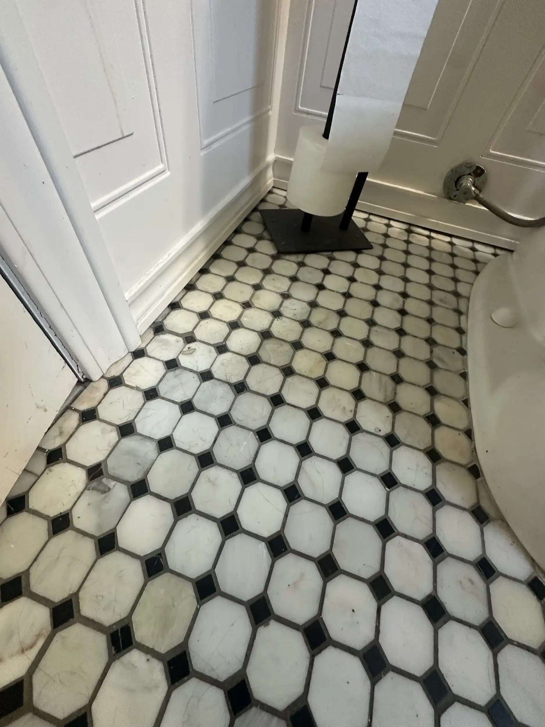 Close-up view of vintage black and white marble hexagonal tile flooring in a bathroom, with a small black rug and a white toilet with a black seat.