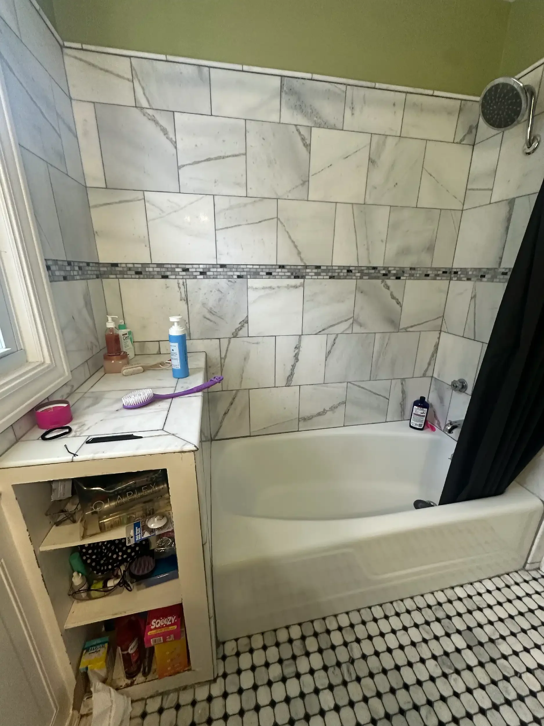 A bathroom shower with marble tiles, shampoo bottles, a grooming brush, and a black shower curtain; a small cabinet with toiletries and a black-and-white hexagonal tile floor.