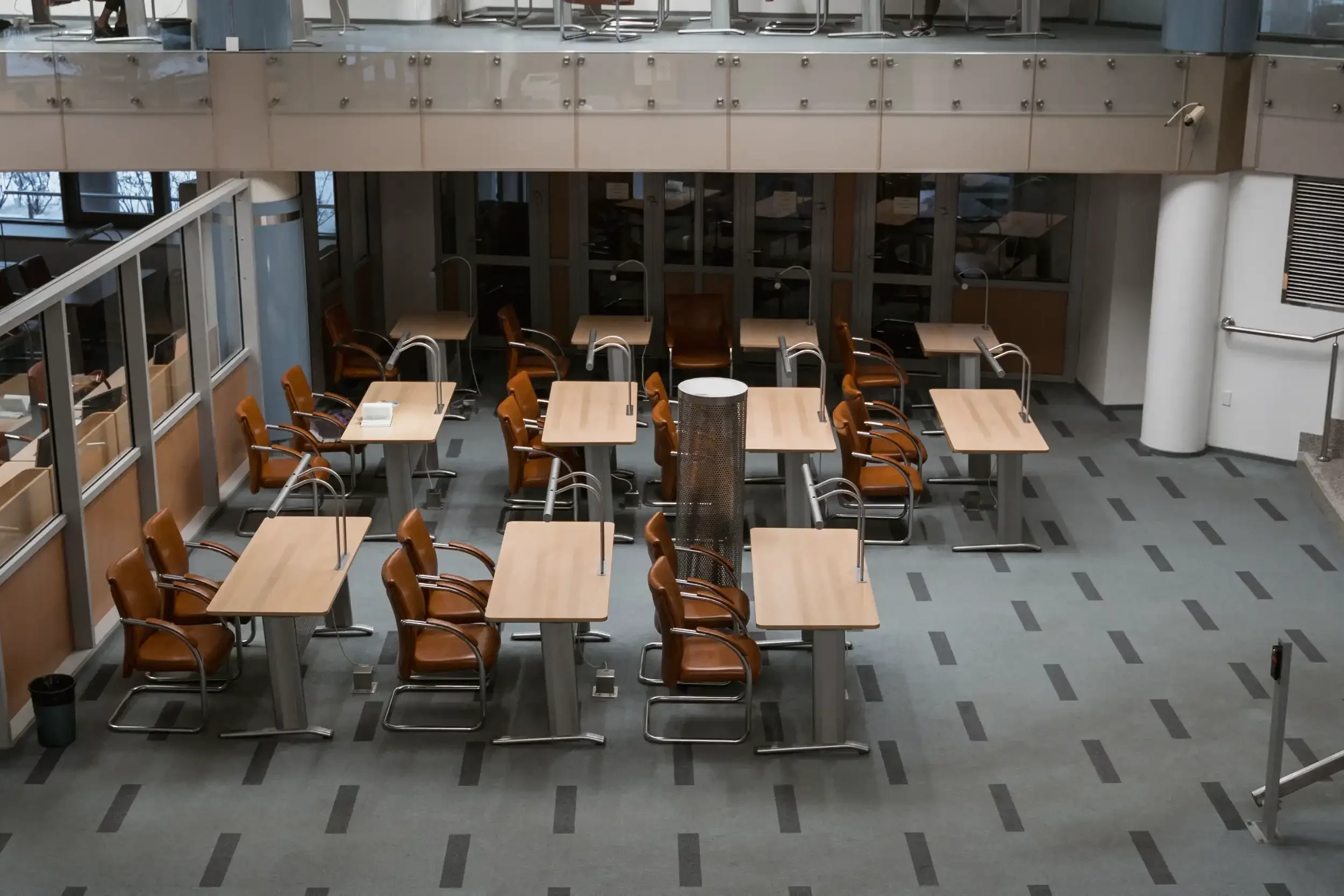 Empty conference or meeting room with multiple tables and brown chairs, glass walls, and large windows in a modern office building.