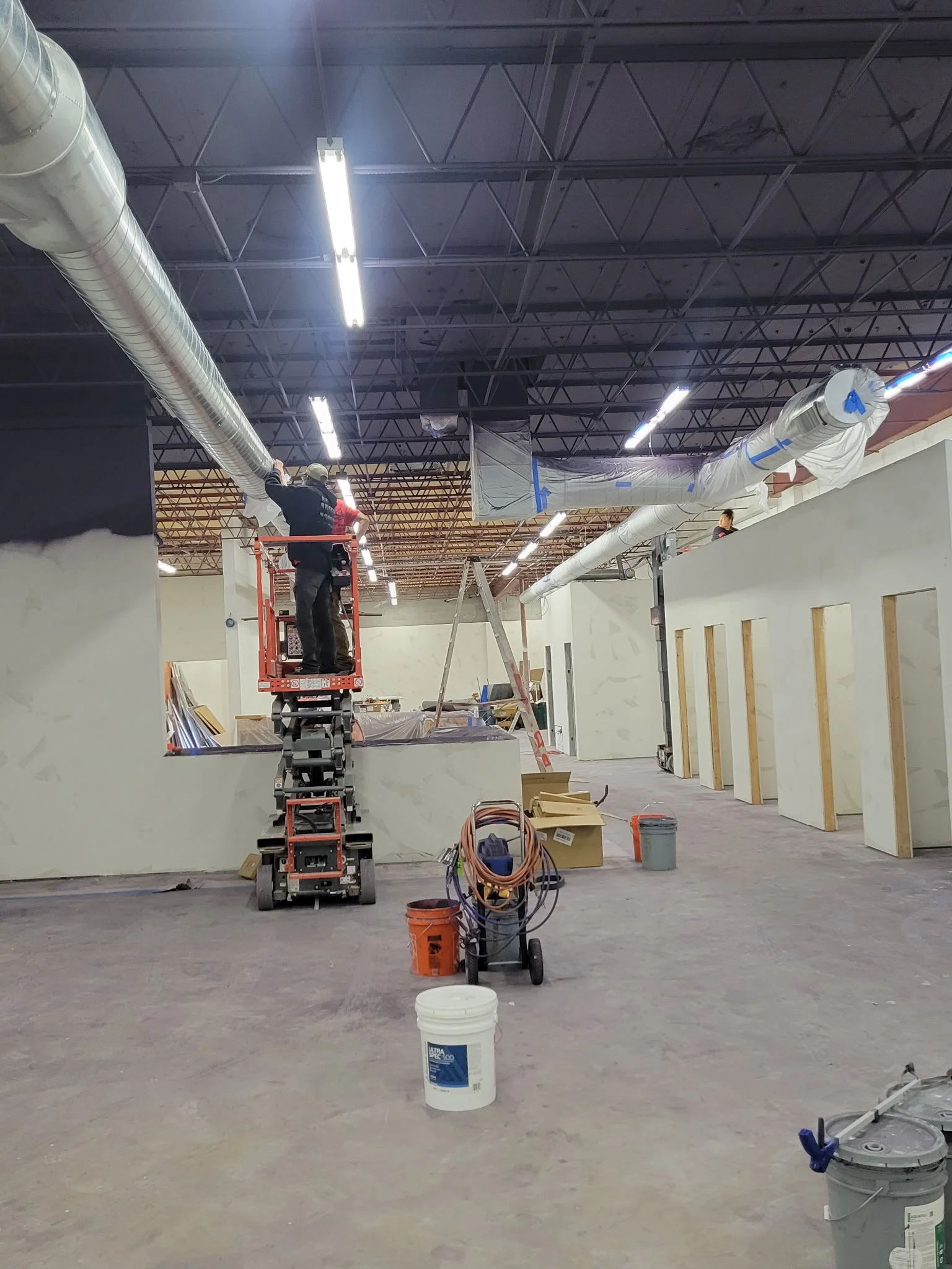 HVAC technicians installing large ductwork in a commercial building with exposed ceiling grid and unfinished walls.