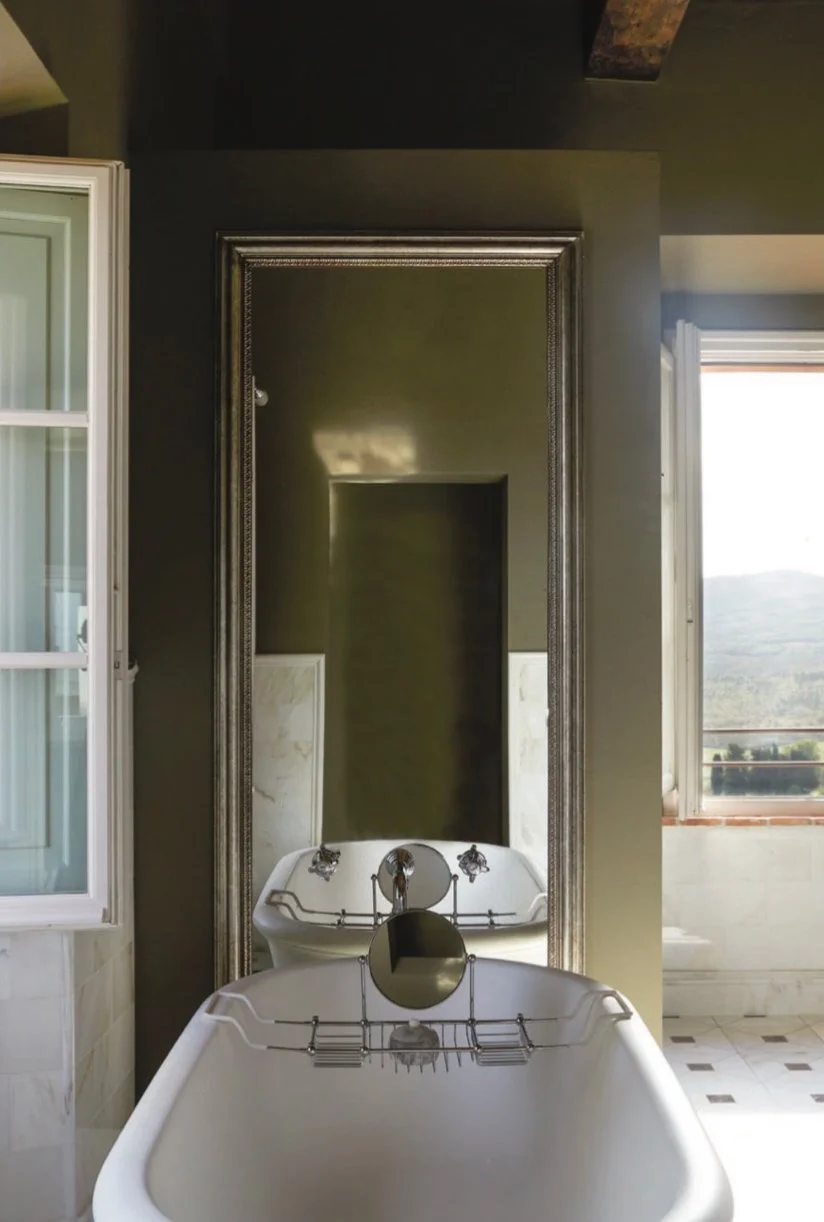 Bathroom with a vintage clawfoot bathtub in front of a large mirror, with a window showing a scenic outdoor view.