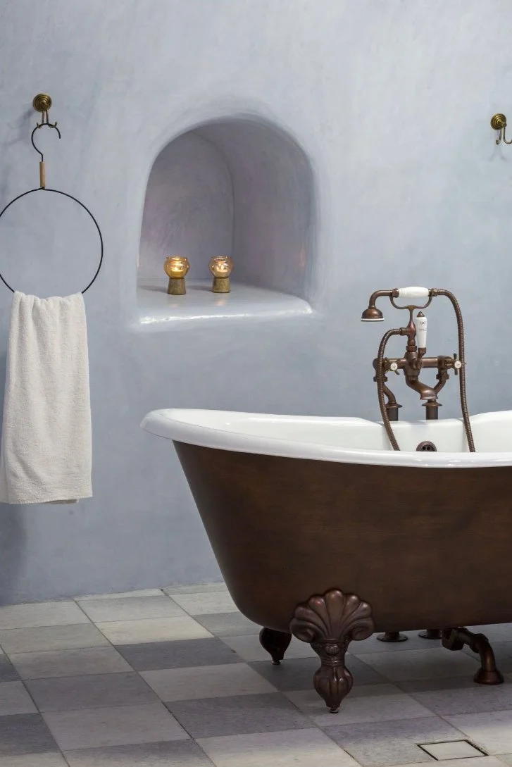 A vintage-style bathroom with a bronze clawfoot bathtub, a white towel hanging on a decorative black ring, and a built-in wall shelf with candles.
