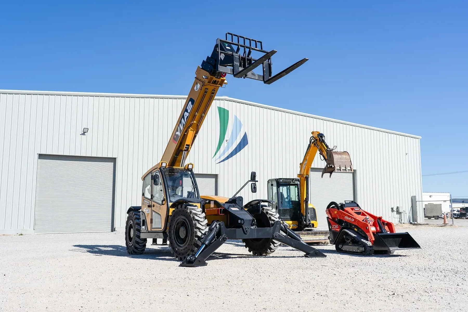 Construction equipment including a telescopic handler, small excavator, and skid-steer loader parked outside a white industrial building with a logo on the wall
