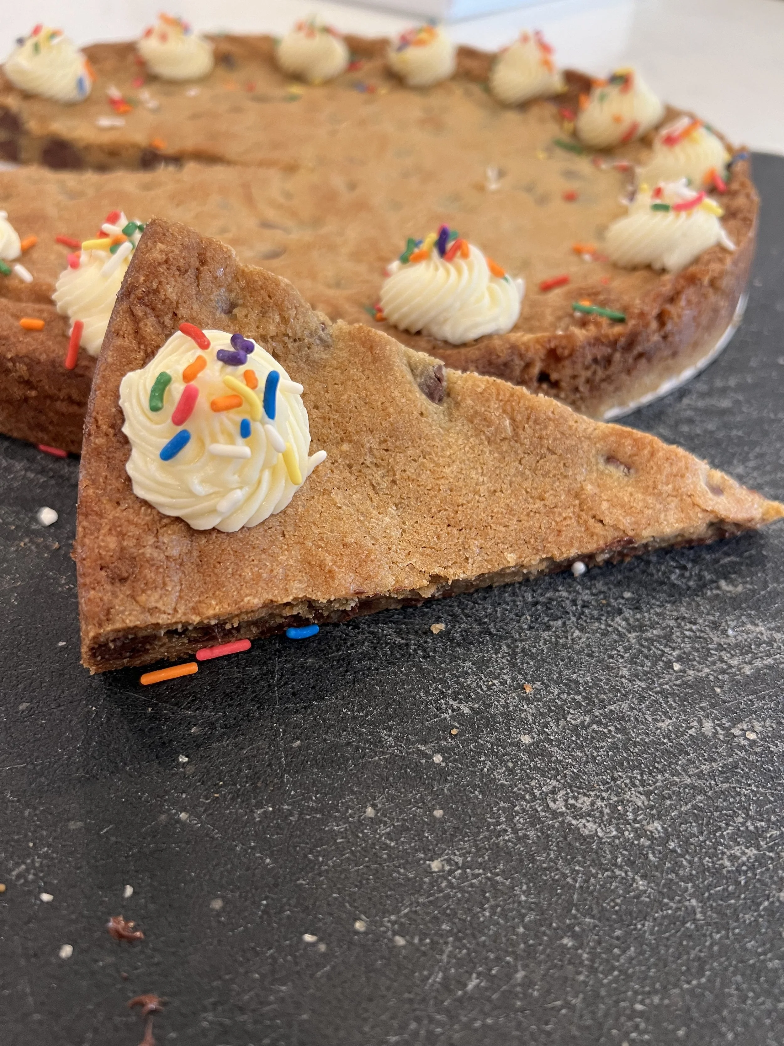 A close-up of a slice of cookie cake with vanilla frosting