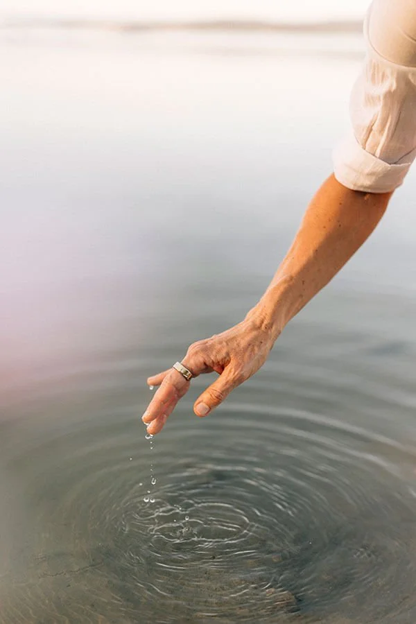 Hand von Anja Mai über dem Wasser mit Wassertropfen.