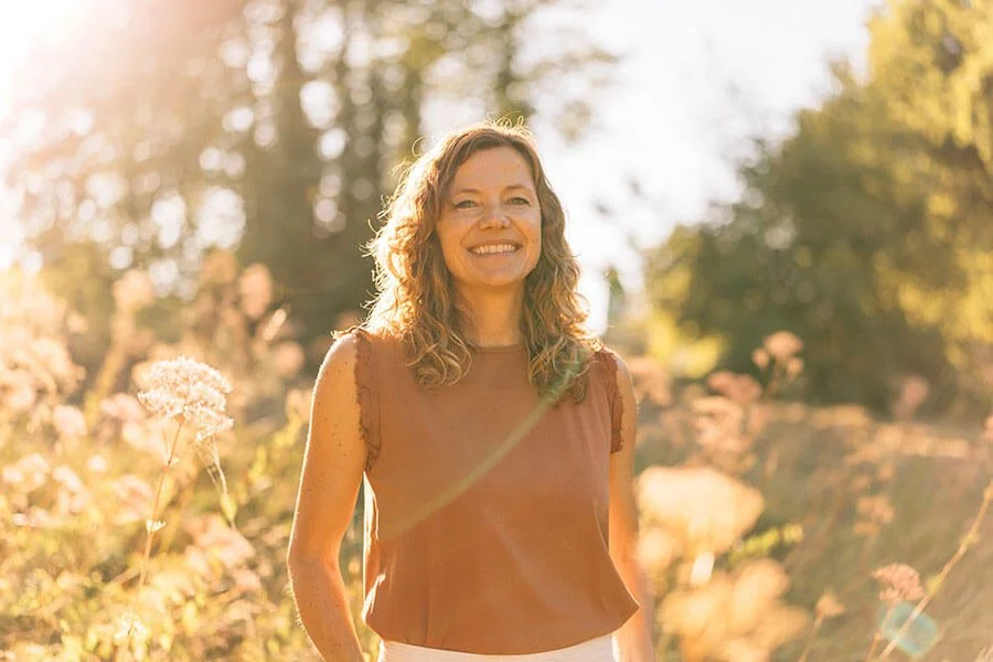 Anja Mai von Bliss, ganzheitliche Therapeutin und Lehrerin für Breathwork in Konstanz. Porträt von ihr in der Natur, sie lächelt in die Kamera, leicht.
