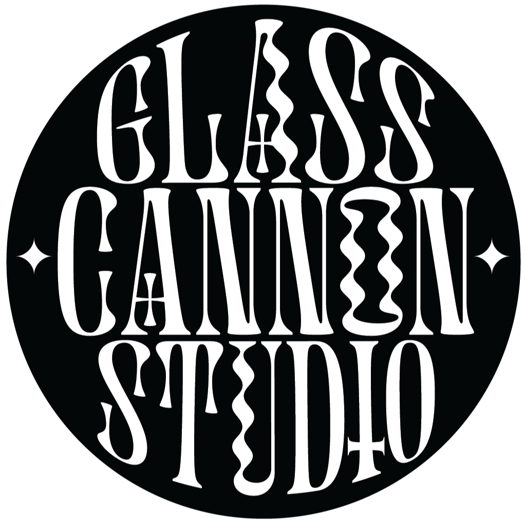 Black circular logo with the words 'Glass Cannon Studio' written in white stylized, elongated, and decorative font, arranged in a circular pattern with small decorative star shapes.
