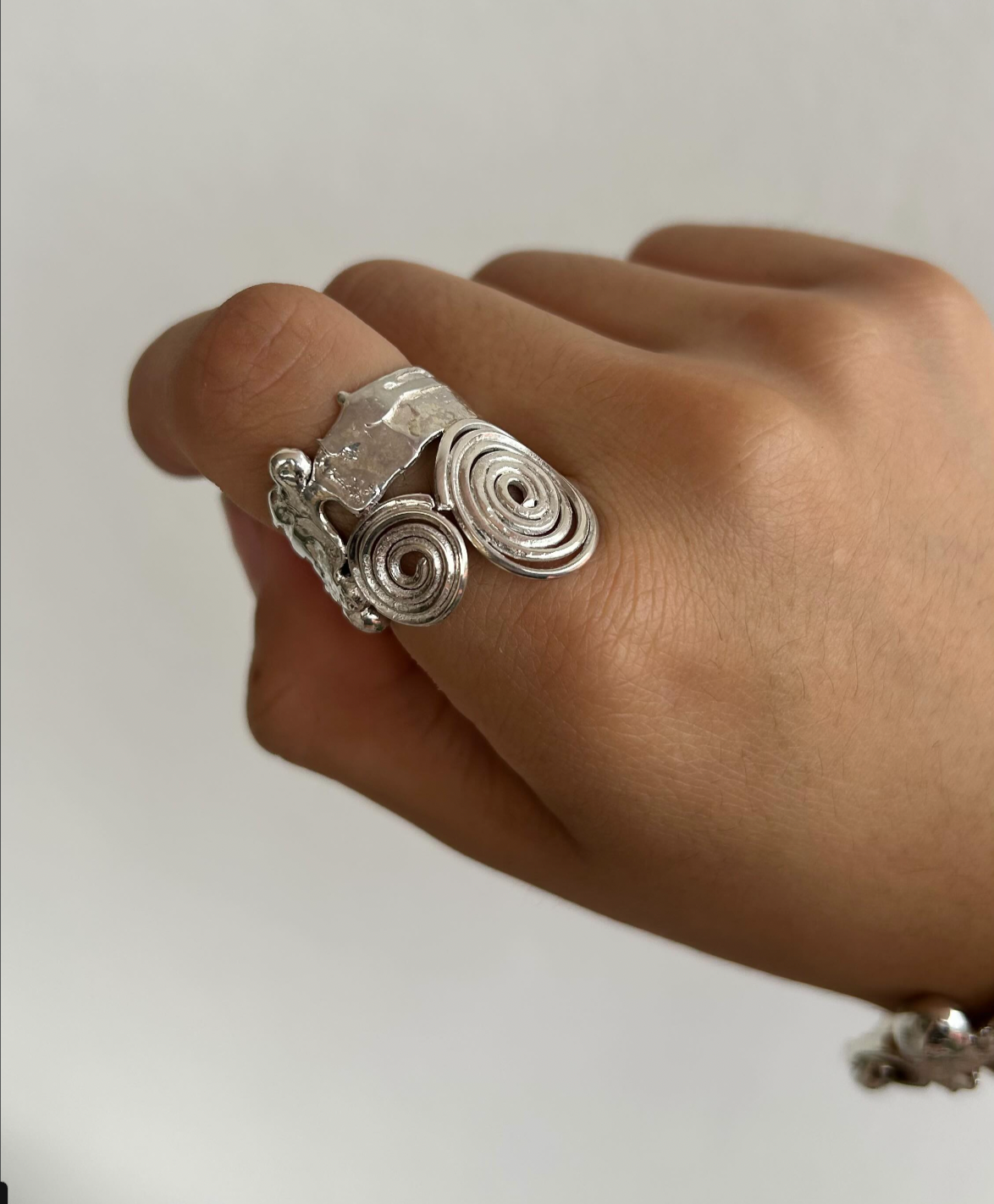 Close-up of a hand wearing a shiny silver ring with intricate spiral and abstract designs against a plain background.
