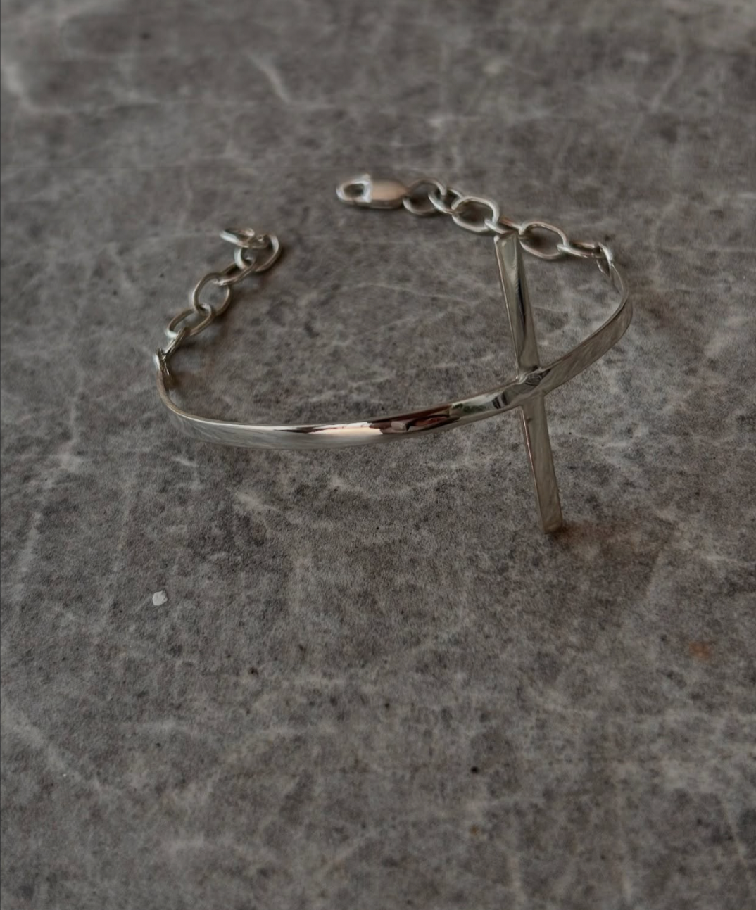 Silver bracelet with a latch and a vertical bar charm, placed on a gray stone surface.