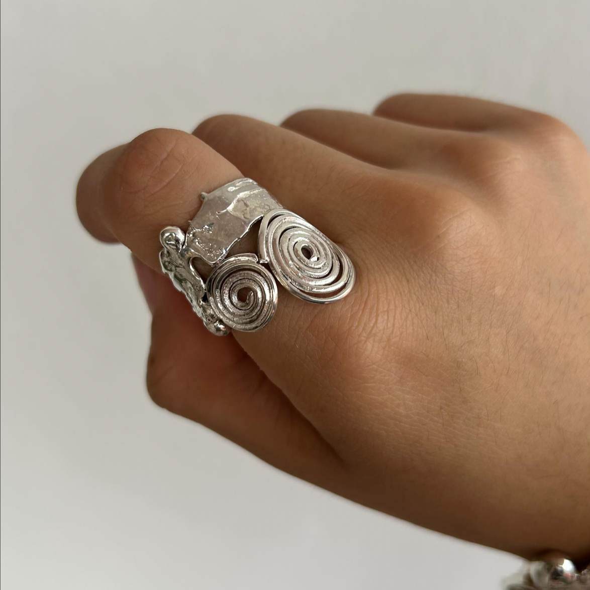 A person wearing a silver ring with spiral designs on their finger.