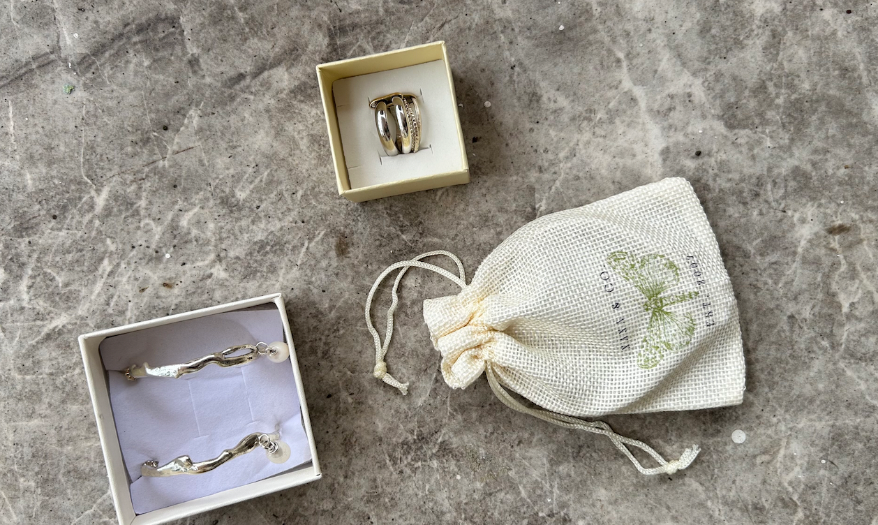 Silver rings in small boxes, one with multiple bands and diamonds, another with a wave design, and a small drawstring pouch on a gray surface.