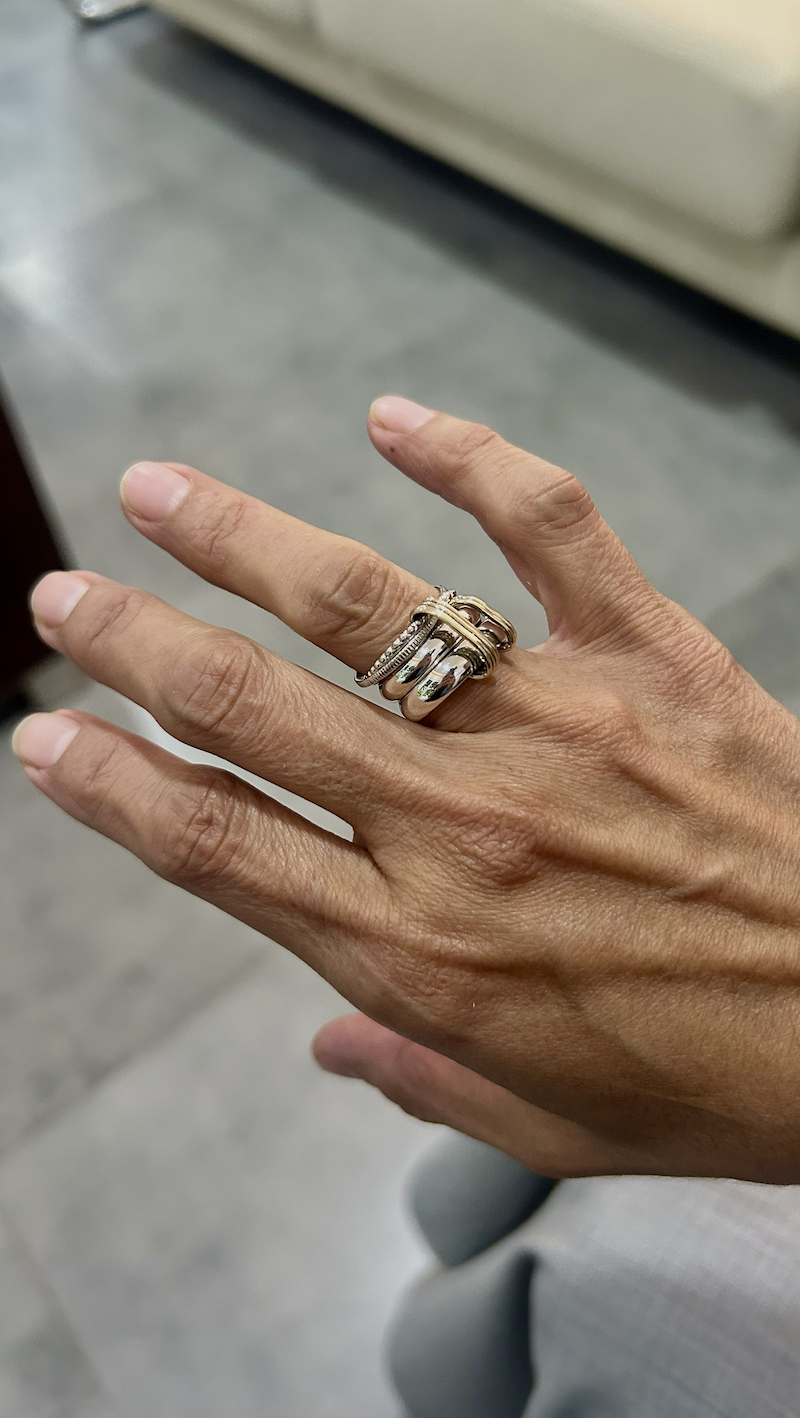 A person's hand showing a silver and gold ring with multiple bands and decorative elements.