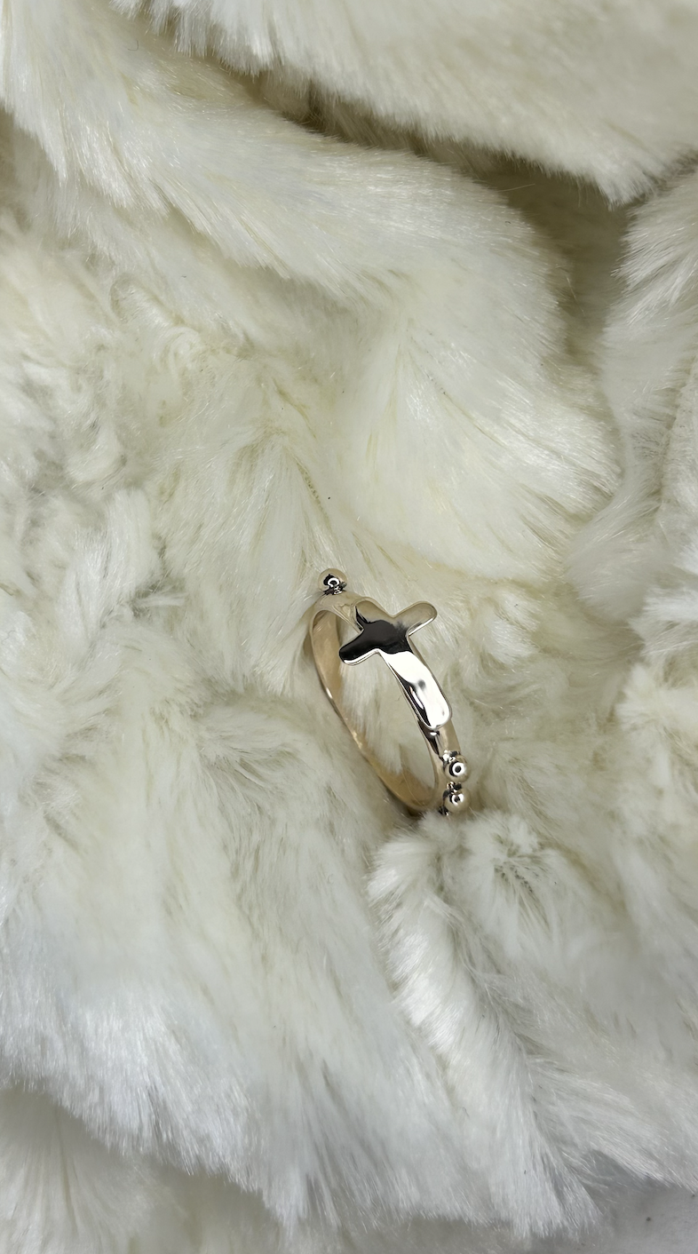 A silver ring with a cross design lying on soft, white, fluffy fabric.