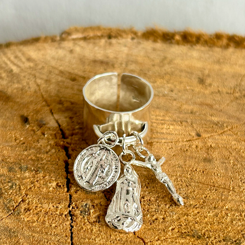 A silver ring with three attached charms lies on a wooden surface.