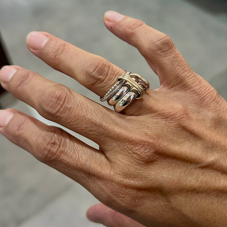 A person's hand wearing multiple silver rings on the middle finger, showcasing jewelry against a blurred background.