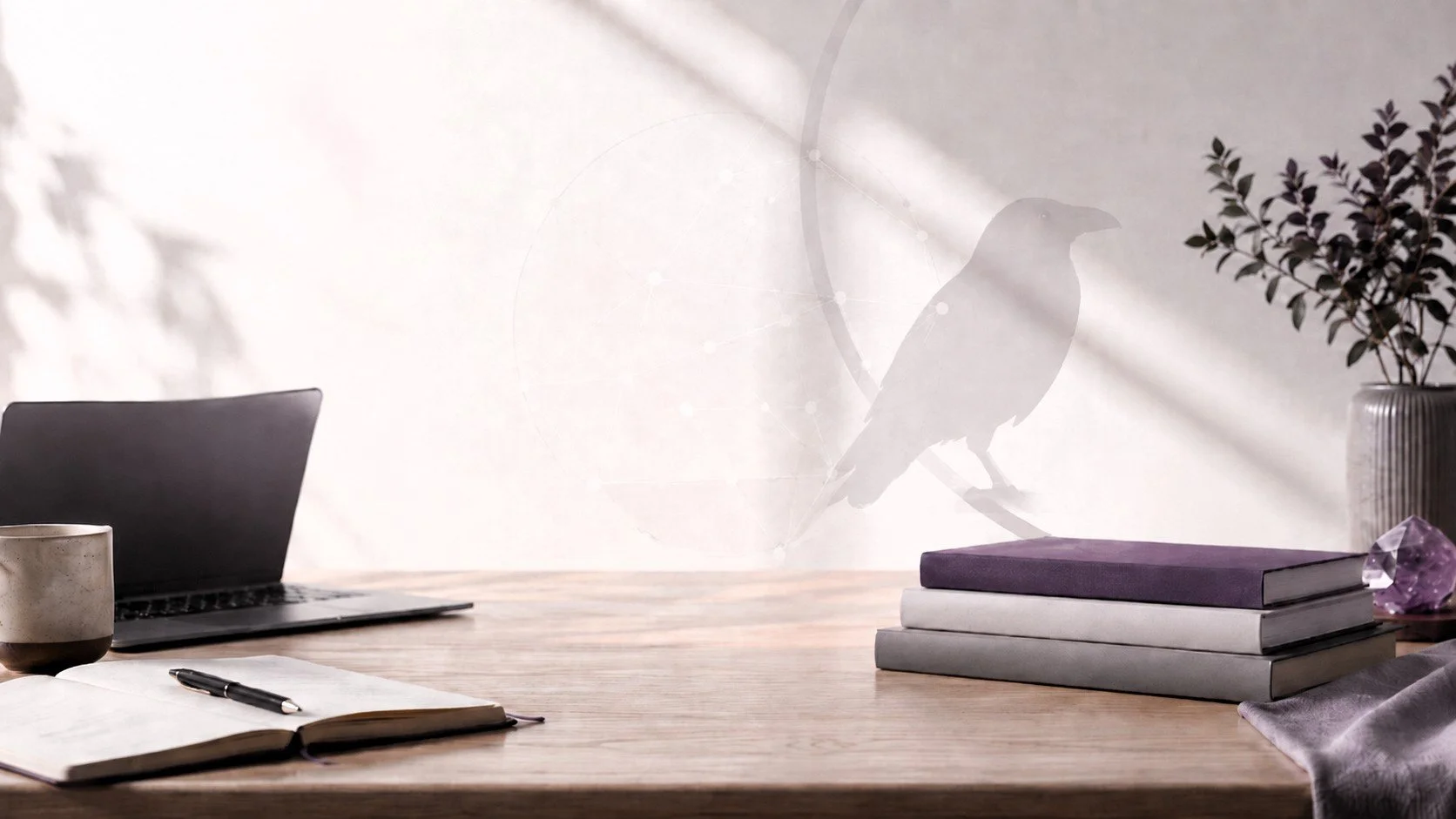A minimalist workspace with an open notebook and pen on a wooden desk, a black laptop, a ceramic mug, three stacked books in shades of gray and purple, a purple gemstone, a gray striped vase with leafy branches, and the shadow of a bird silhouette on a white wall with soft natural light.