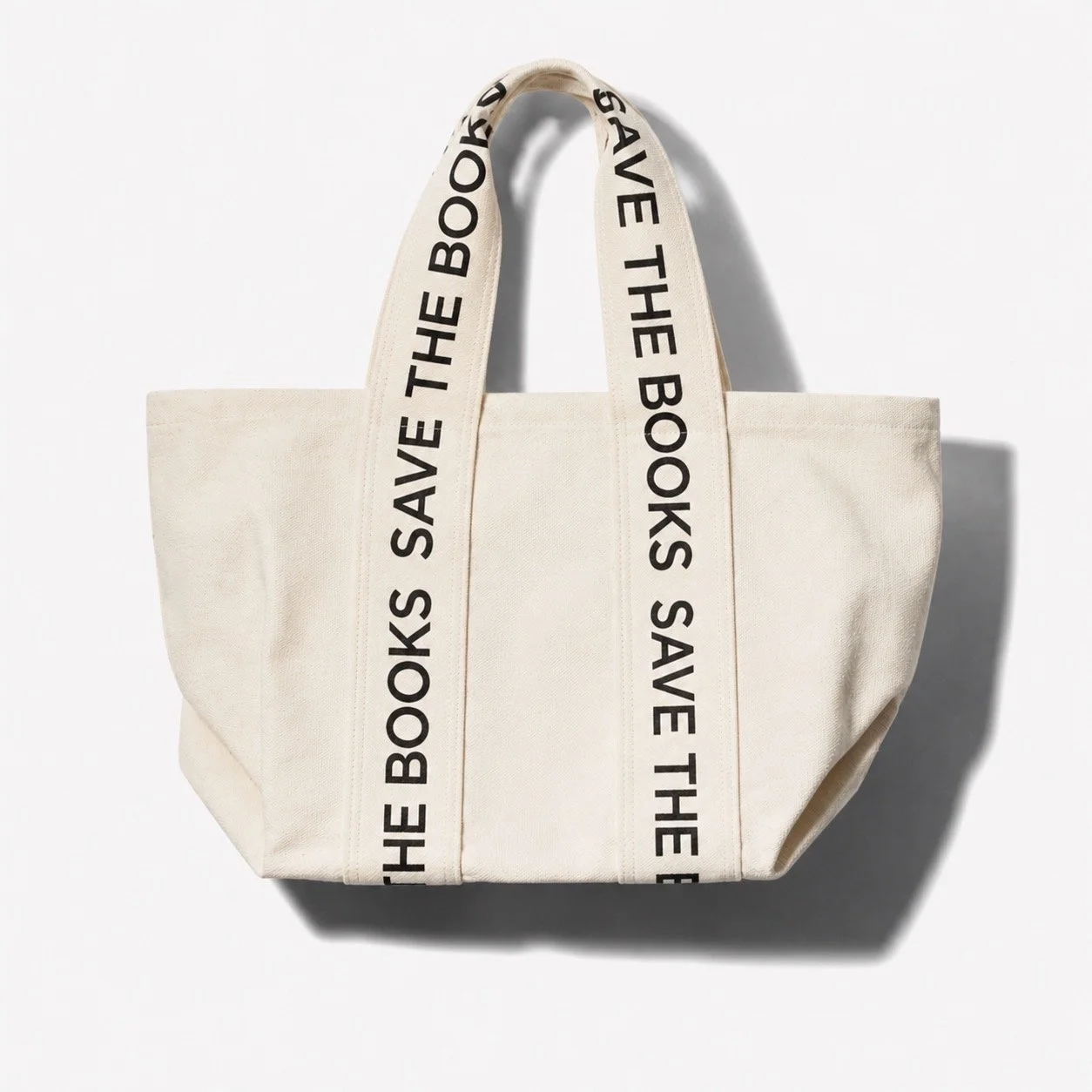 White tote bag with black writing on the straps that says 'SAVE THE BOOKS' set against a white background.