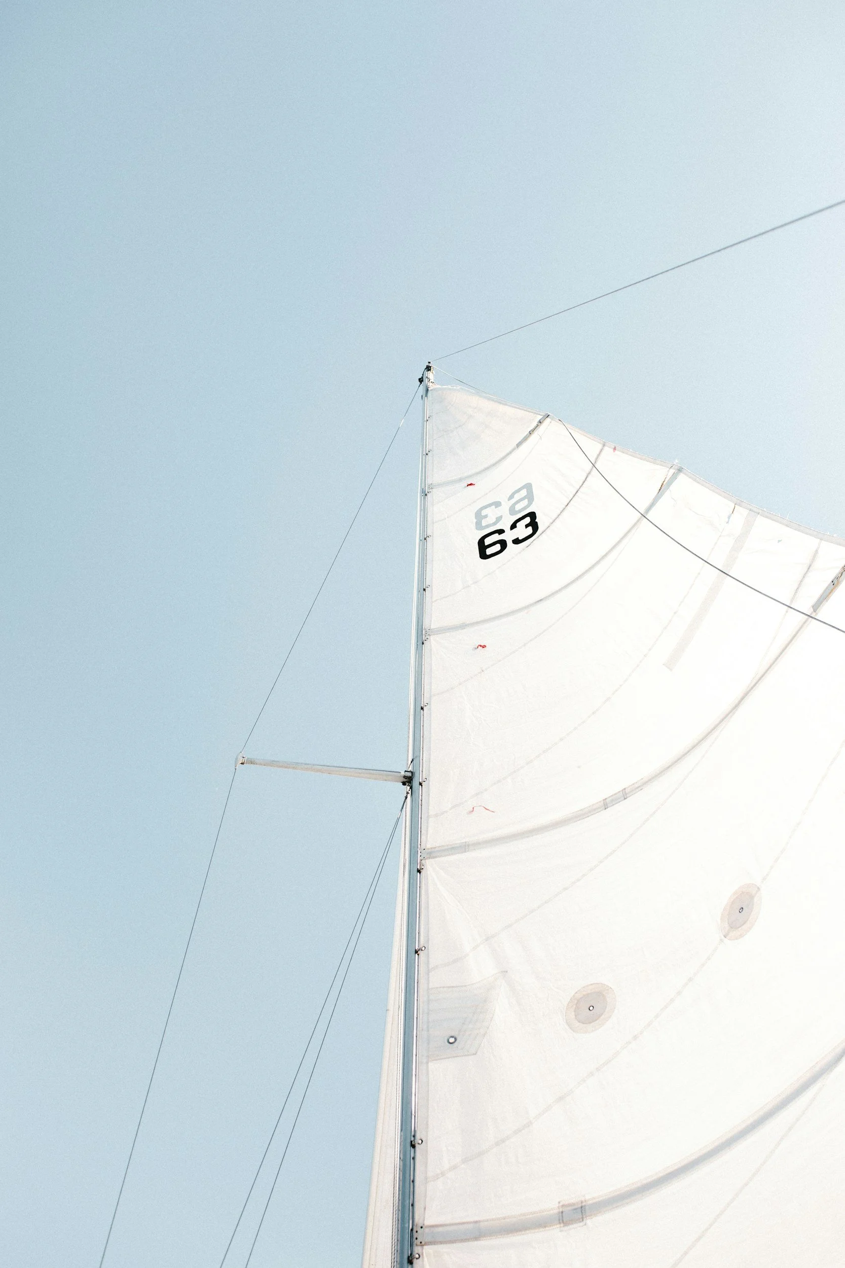 Close-up view of a sailboat's sail against a clear blue sky, with the sail marked 'C3 63'.