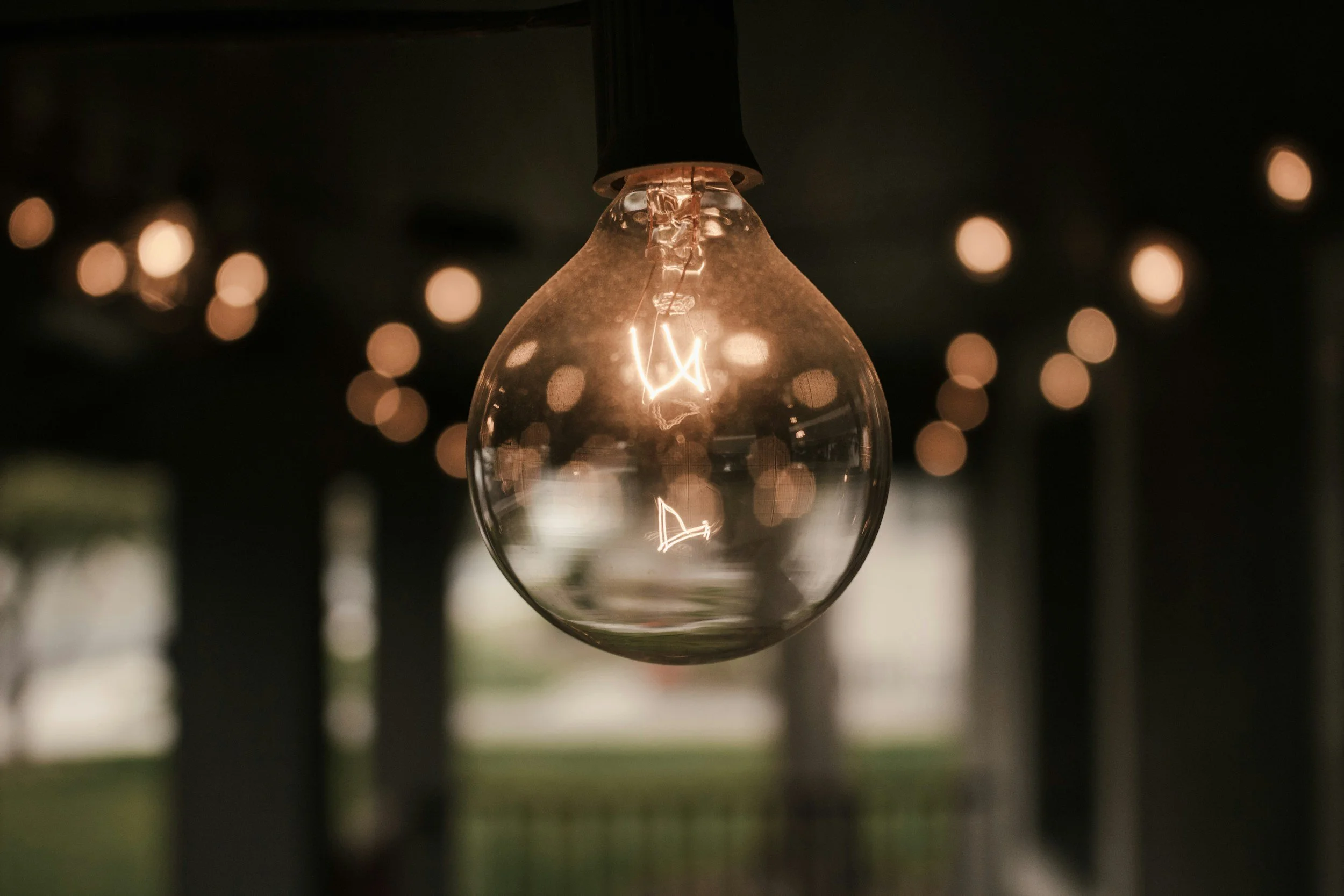 Close-up of an incandescent light bulb hanging, with blurred background lights creating a bokeh effect.