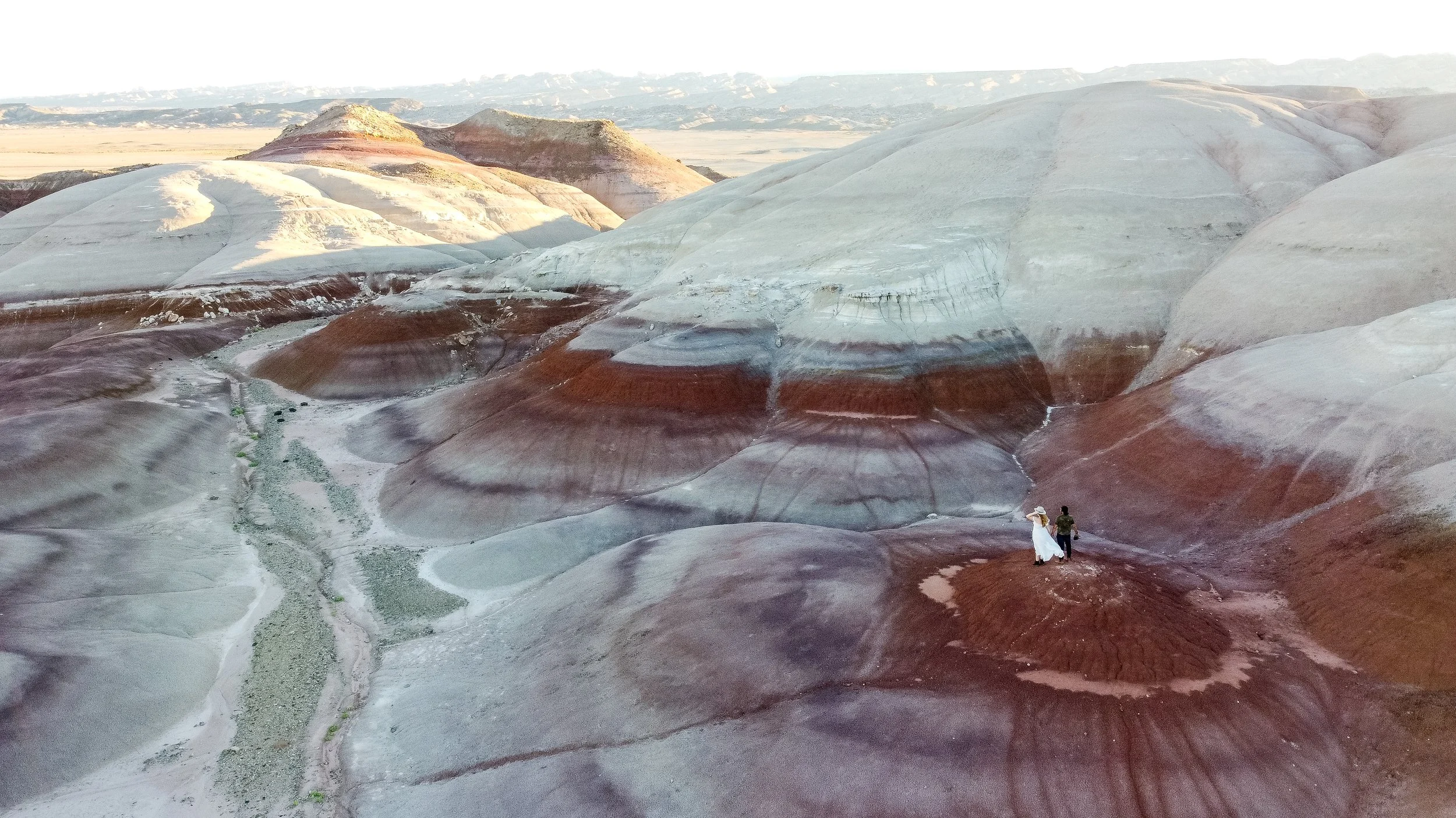A couple walking on colorful layered rock formations in a desert landscape.