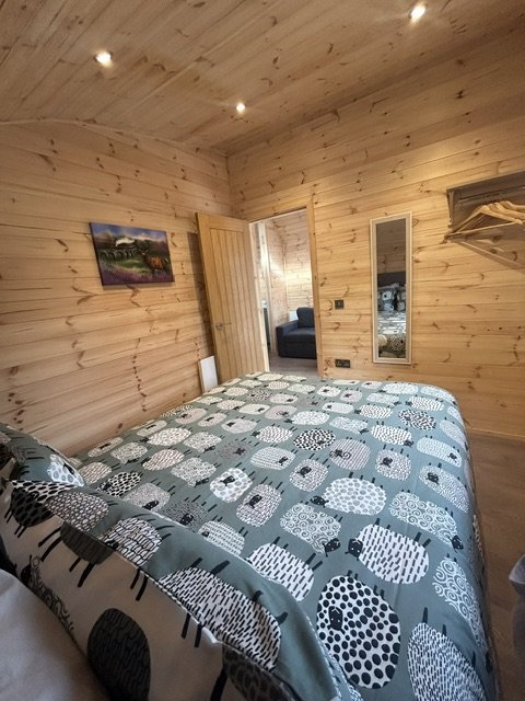 Wood-paneled bedroom with a bed featuring a black and white patterned duvet and pillows, a mirror on the wall, and a small door leading to another room.