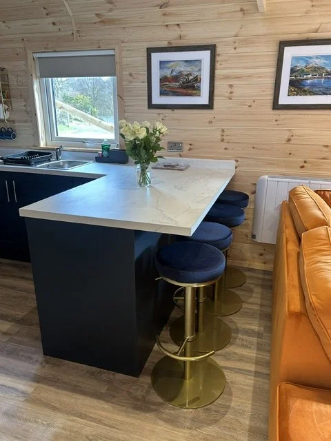 A kitchen counter with stools, a vase of white flowers, and paintings on a wooden wall.