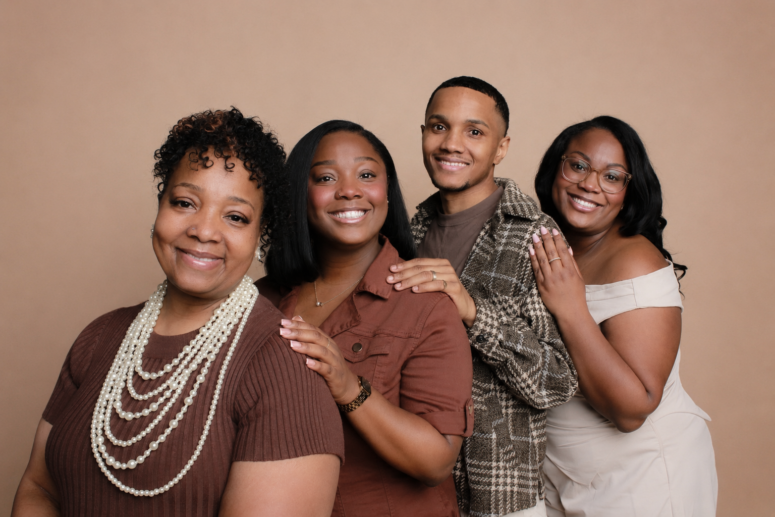 Four women standing closely together, smiling for the camera against a beige background.