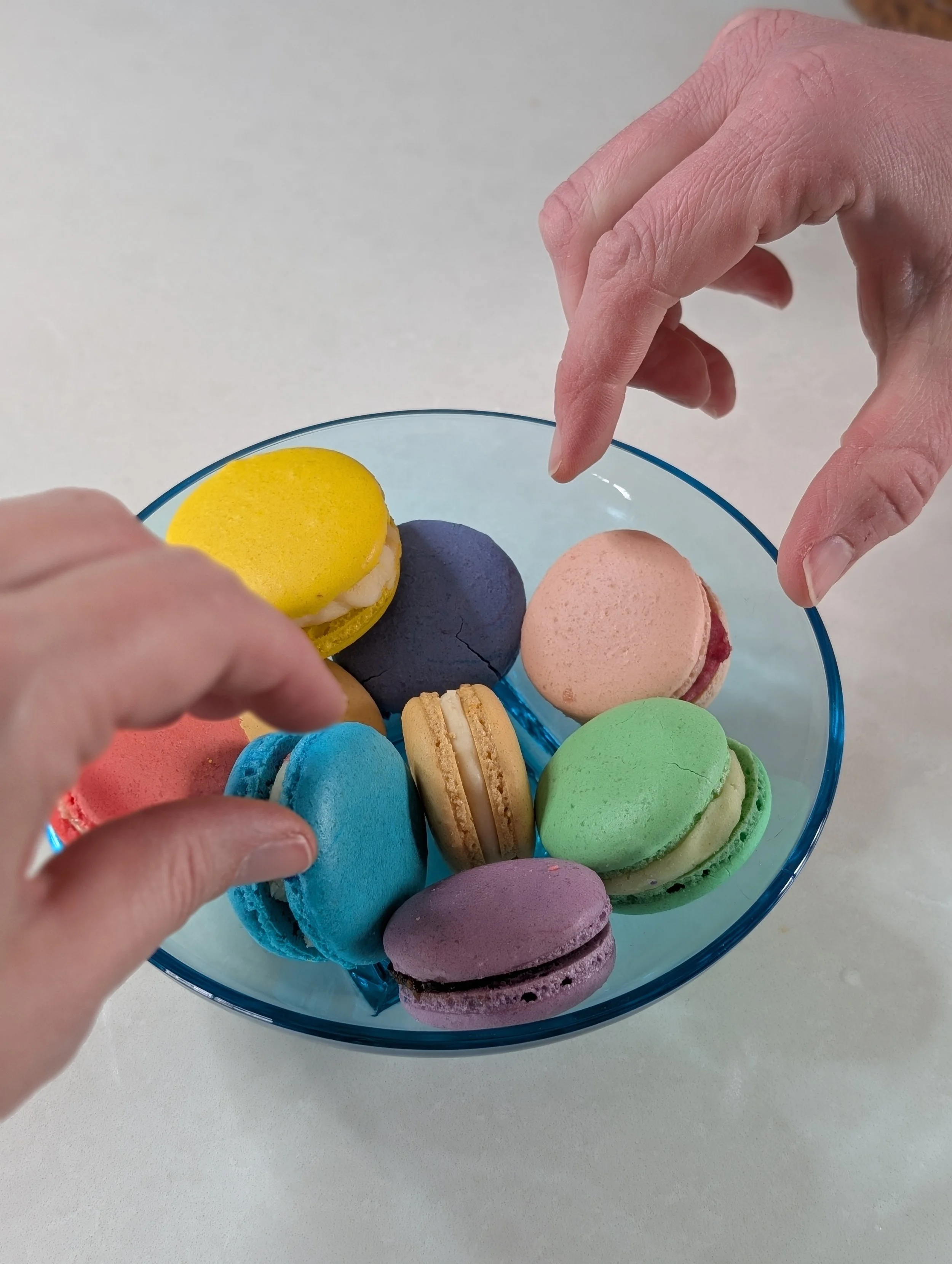 Carpe Macarons Hands Reaching for Macarons From Blue Plate