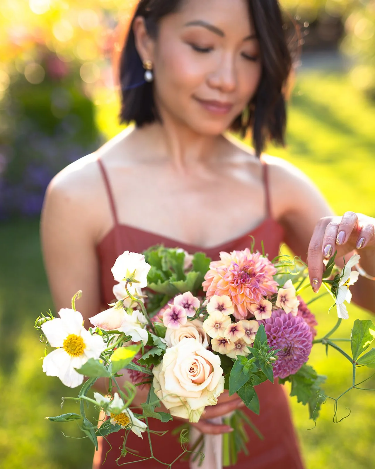 A woman in a red dress holding a colorful bouquet of flowers outdoors during daylight.