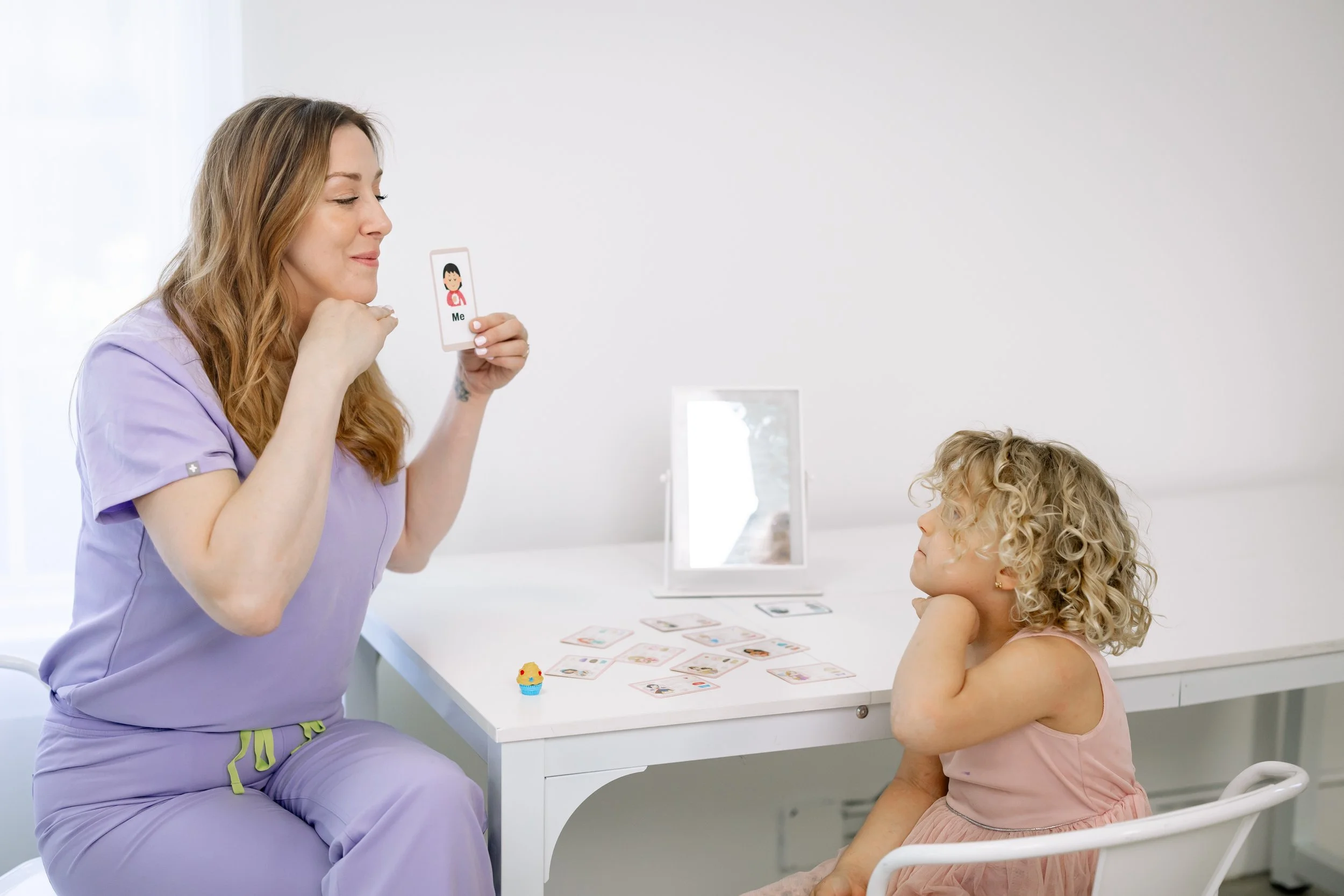 Dr. Jenn Moore using picture cards during a pediatric speech therapy session with a young child.