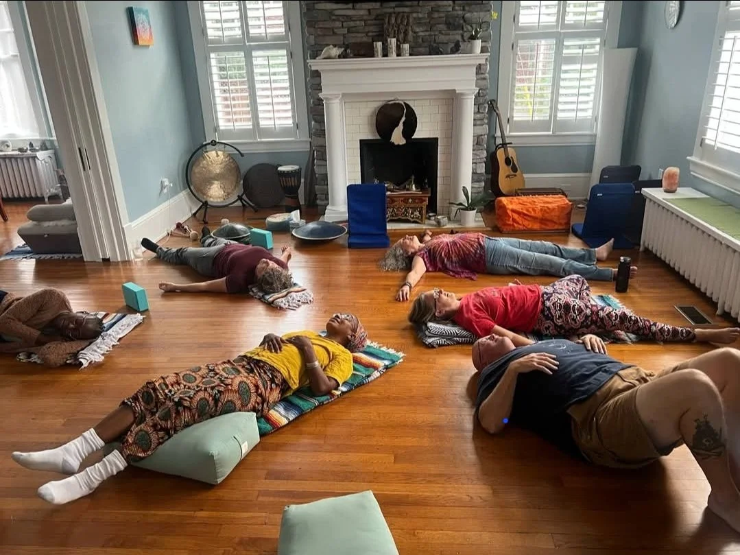 People practicing yoga in a living room with hardwood floors, a fireplace, and large windows with shutters.
