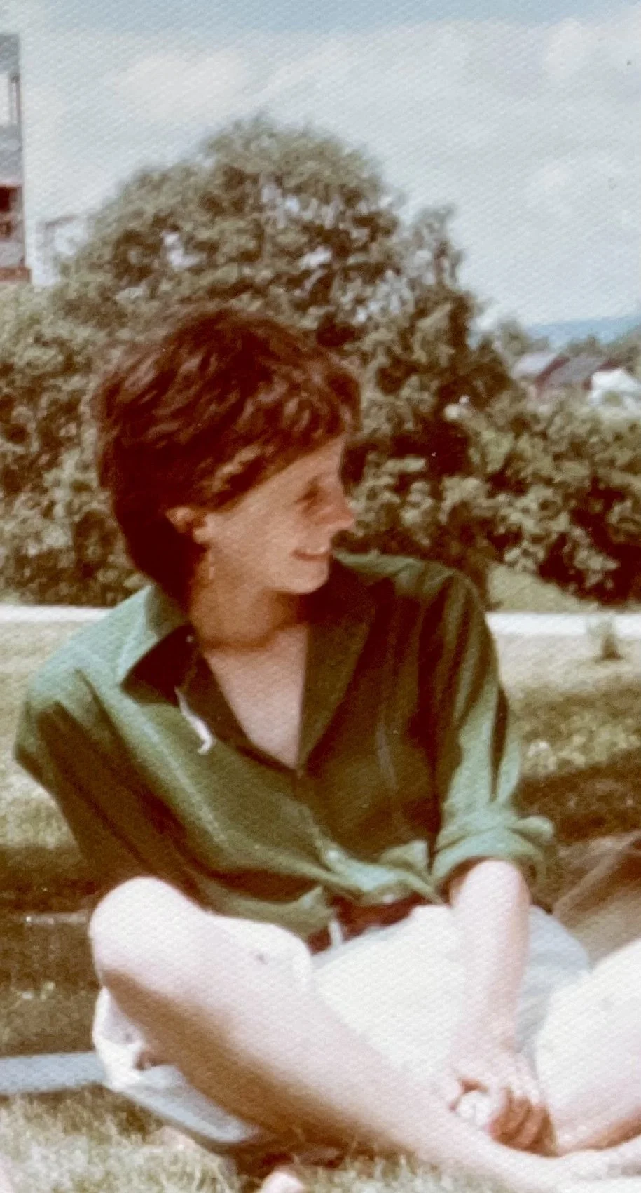 judith mcdaniel grainy image of karen clark in green shirt sitting down cross legged and smiling on a sunny day