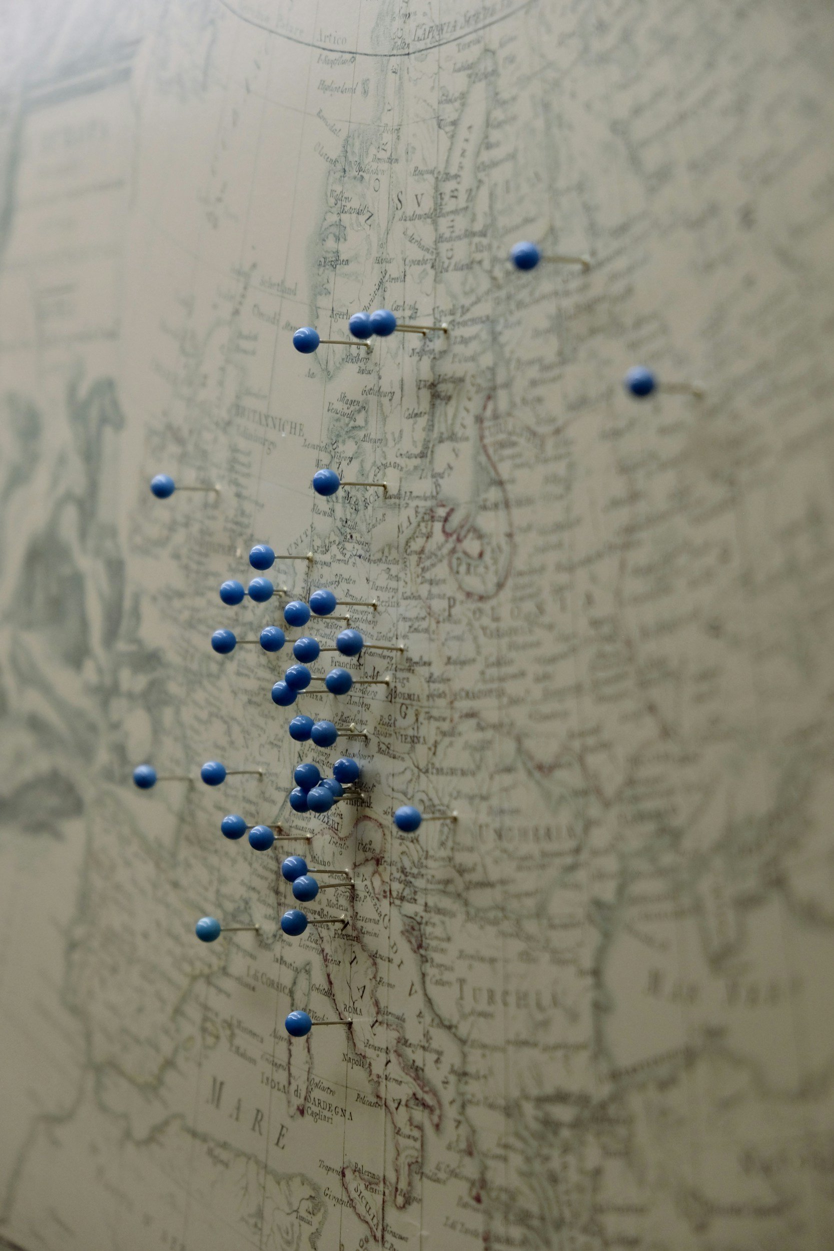A vintage map of Italy with numerous blue pushpins marking locations along the country.