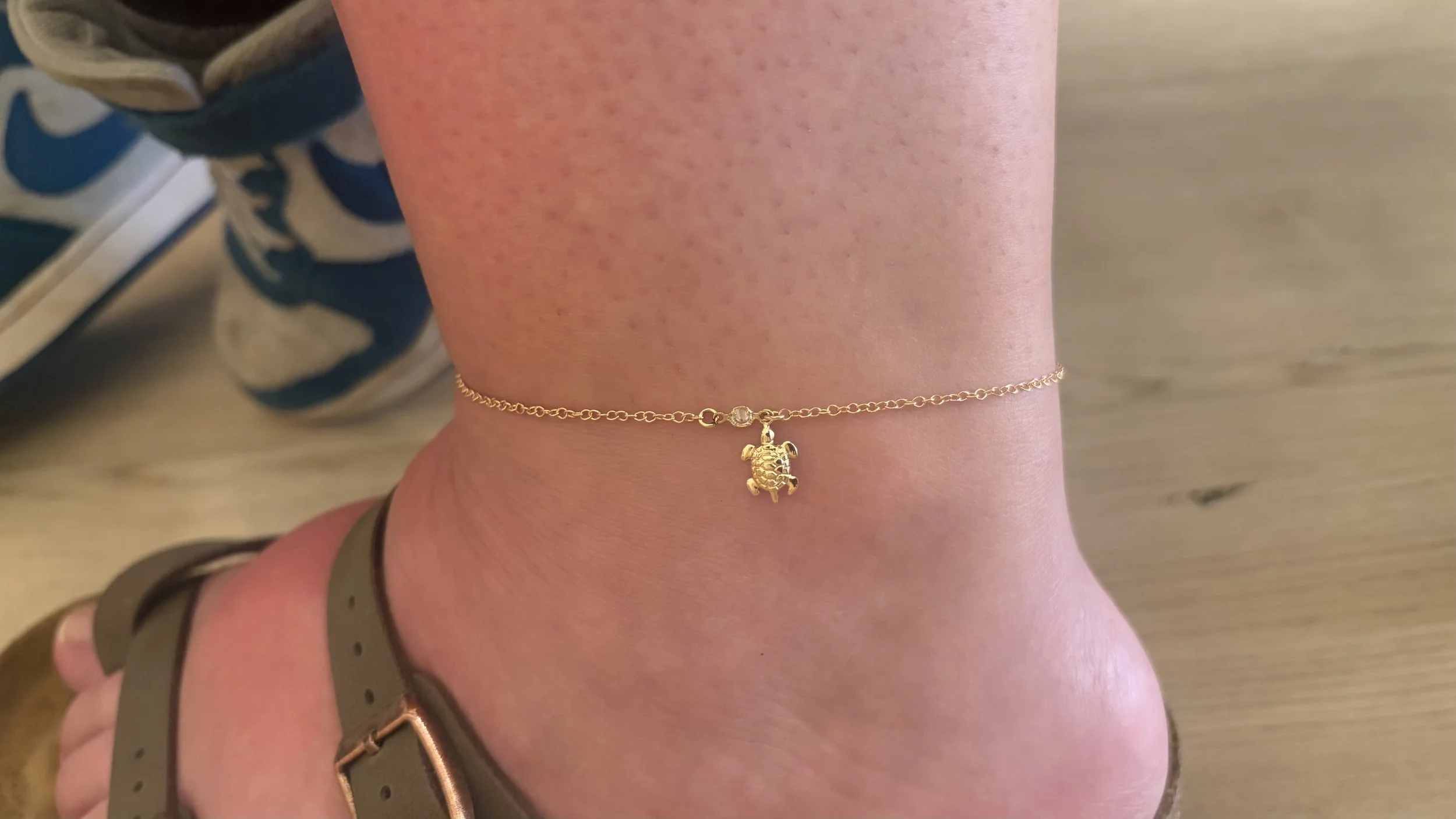 Gold anklet with a turtle charm worn around a person's ankle.