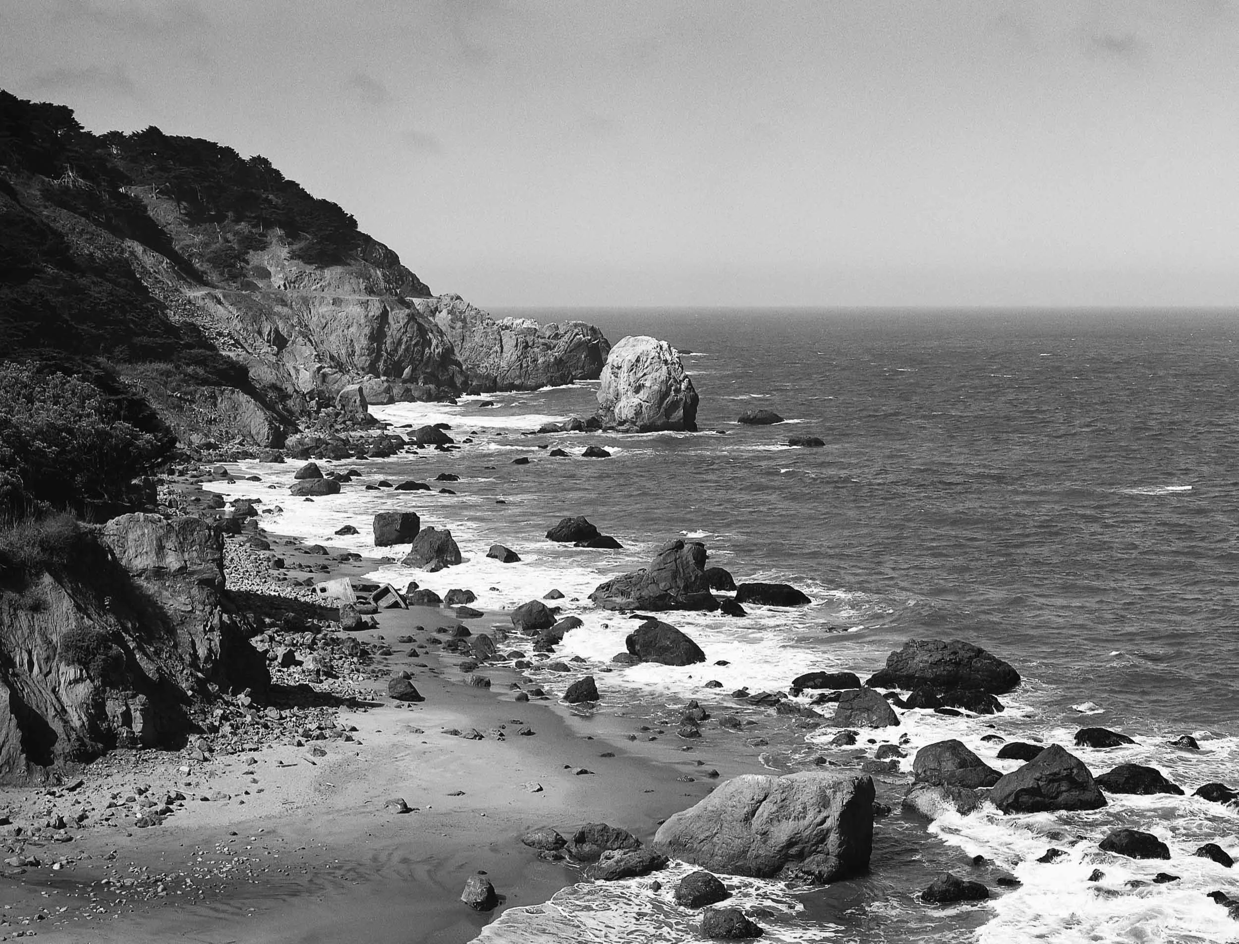 Black and white photo of a rocky coastline with cliffs and ocean waves.