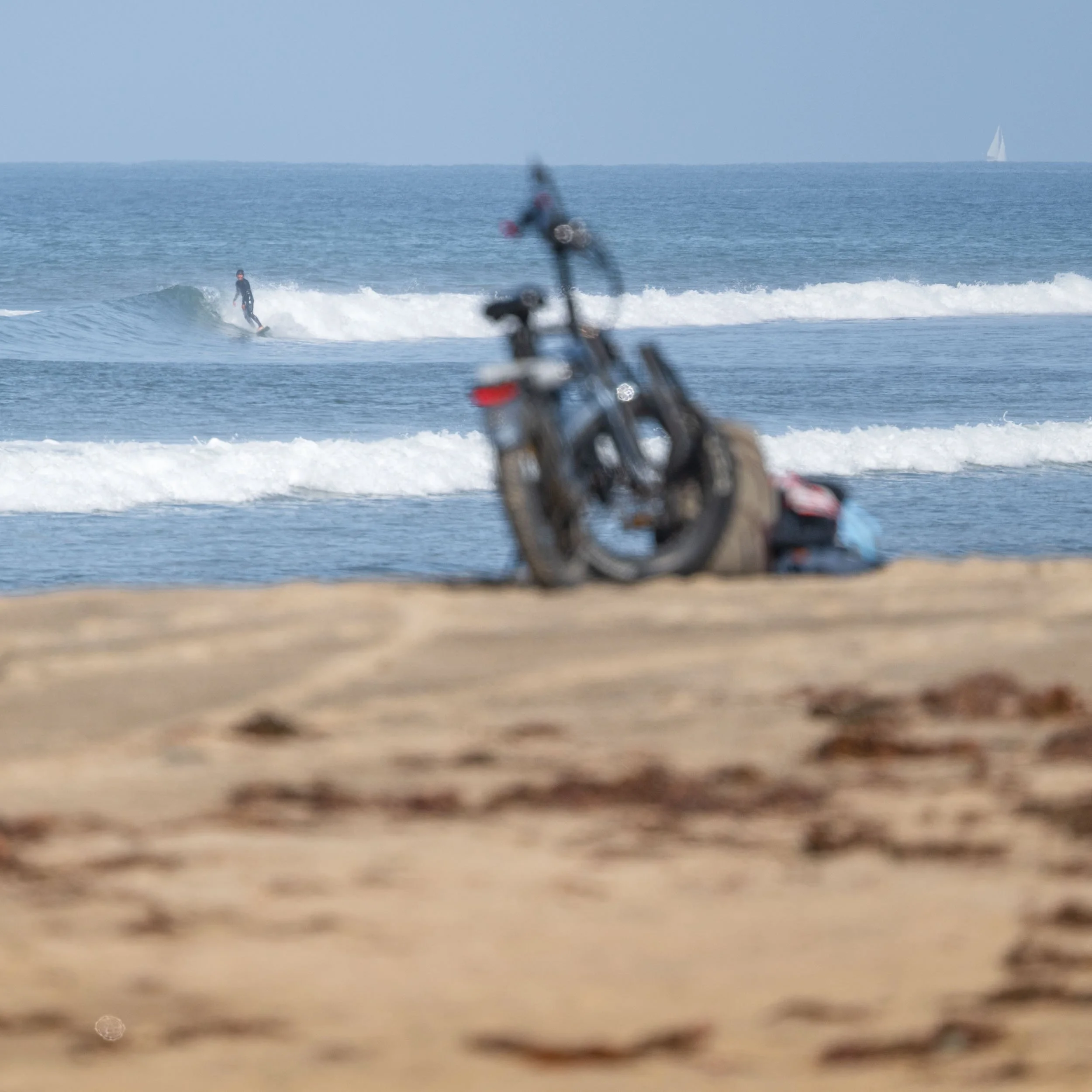 A person surfing on a wave at the beach, with bicycles in the blurred foreground.