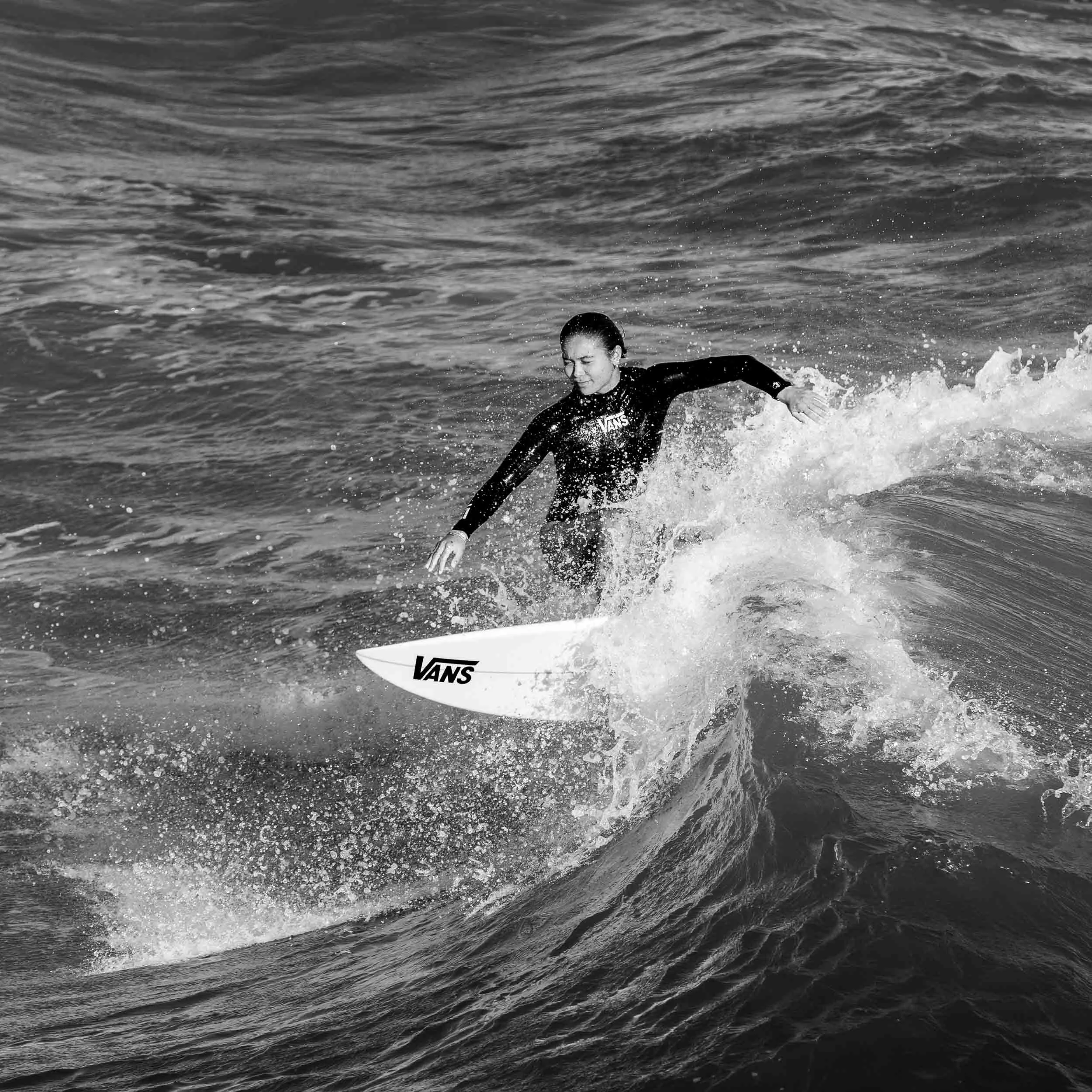 A woman wearing a wetsuit and holding a surfboard standing in the ocean with waves around her.