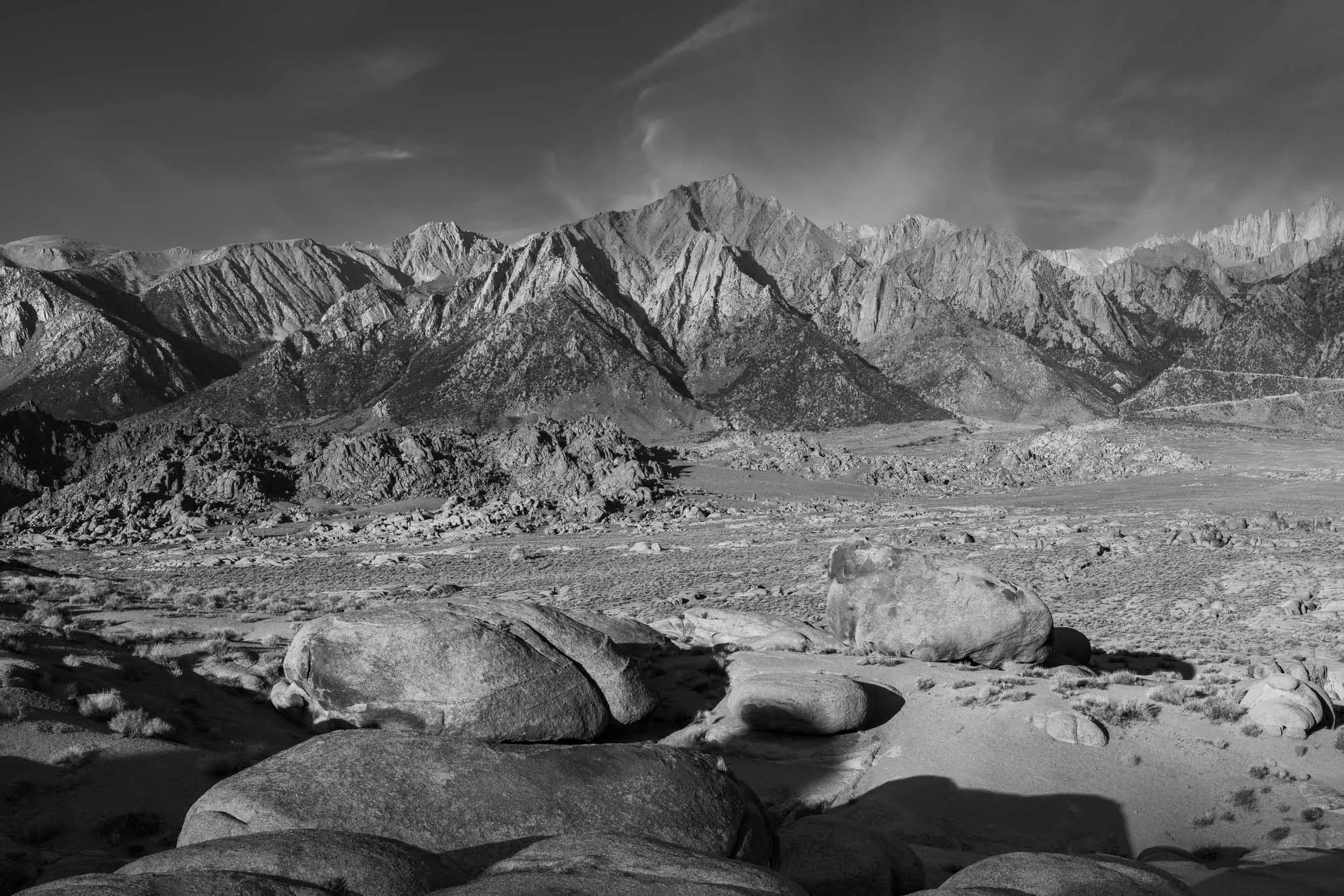 Black and white photograph of rugged mountain range with rocky terrain in the foreground in Alabama Hills